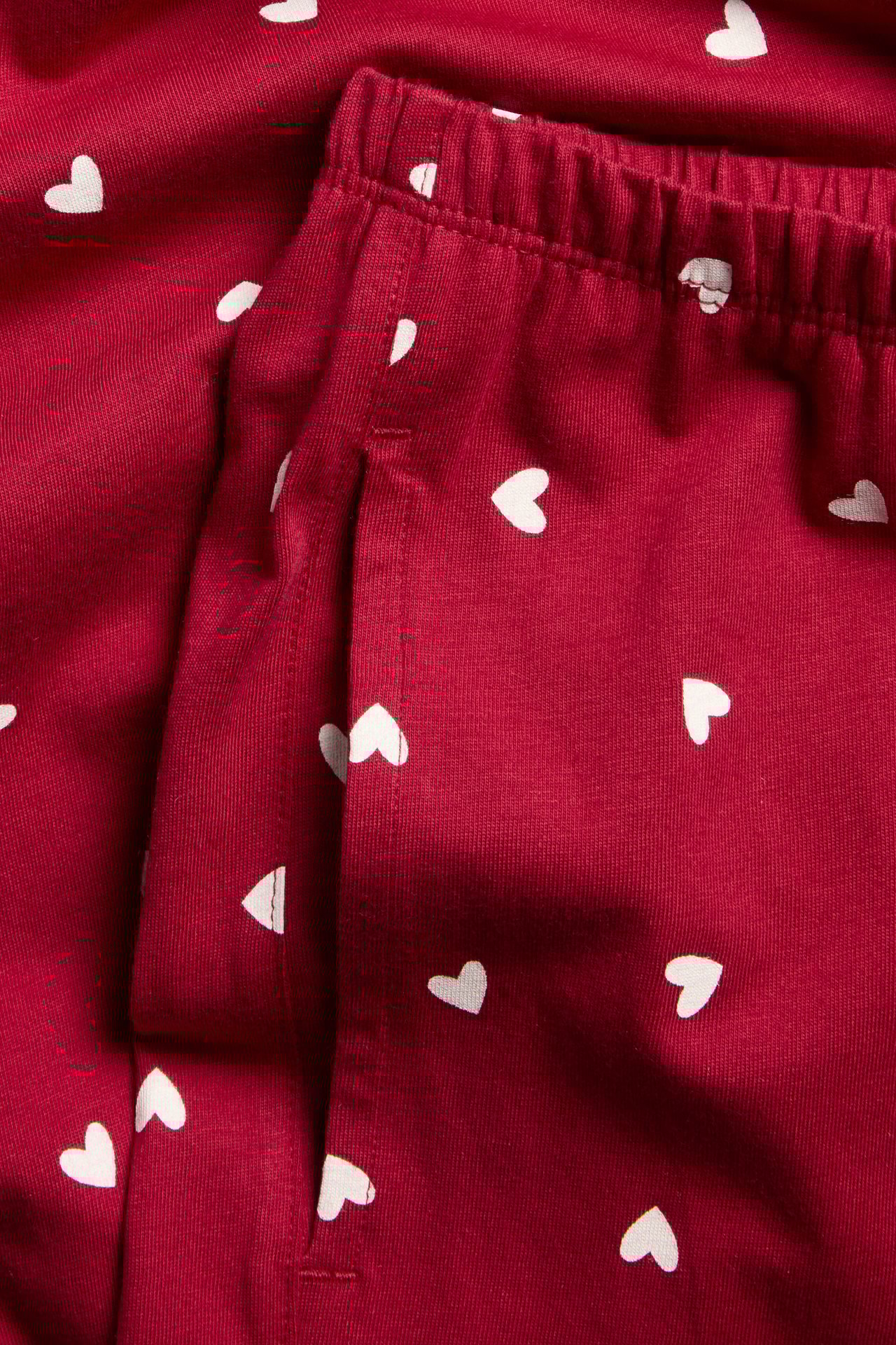 Närbild av röda pyjamasbyxor i bomullsjersey med vitt hjärtmönster, resår i midjan och sidfickor.