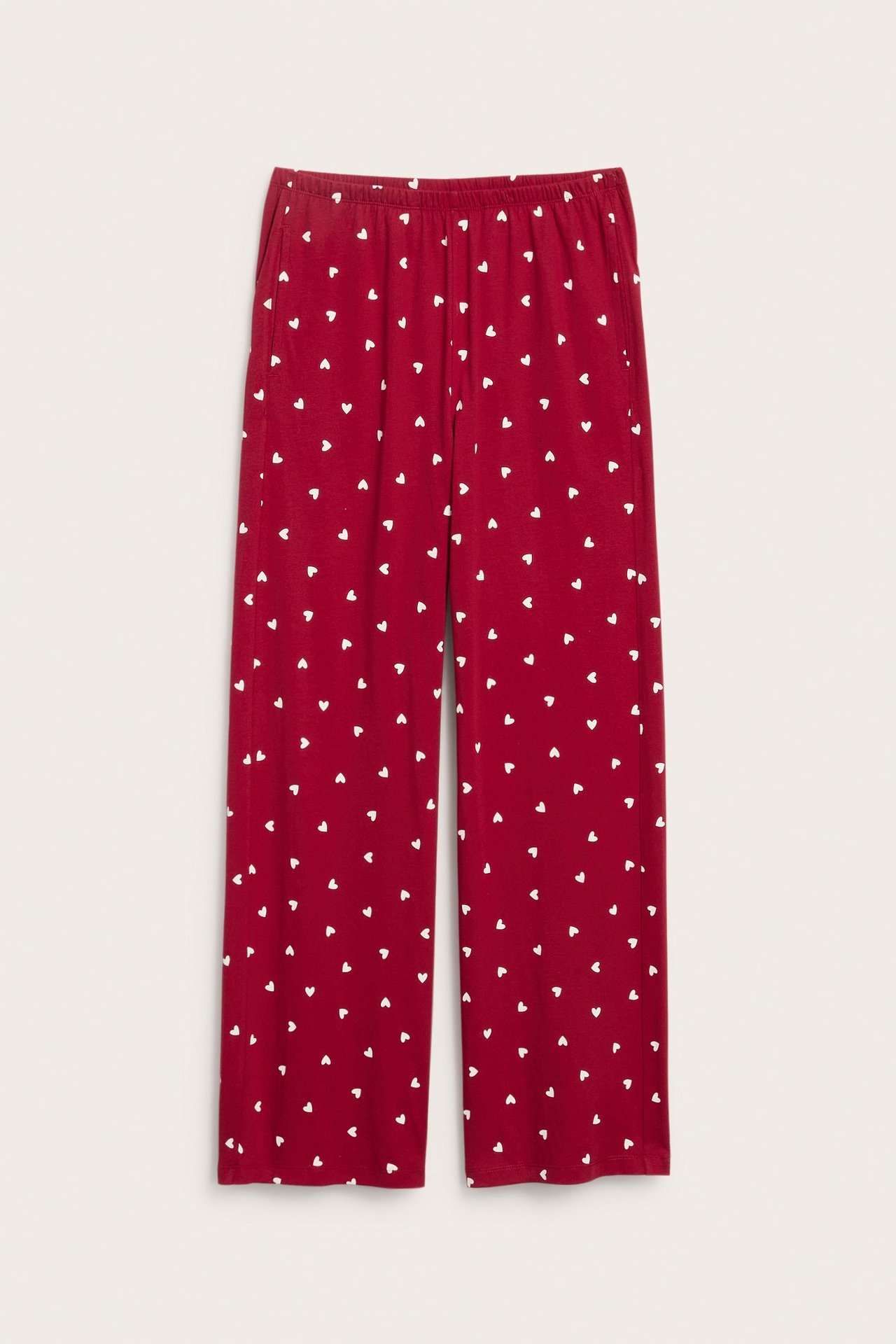 Frontbilde av rød jersey-pyjamasbukse med hvitt hjertemønster, elastisk midje og sidelommer.