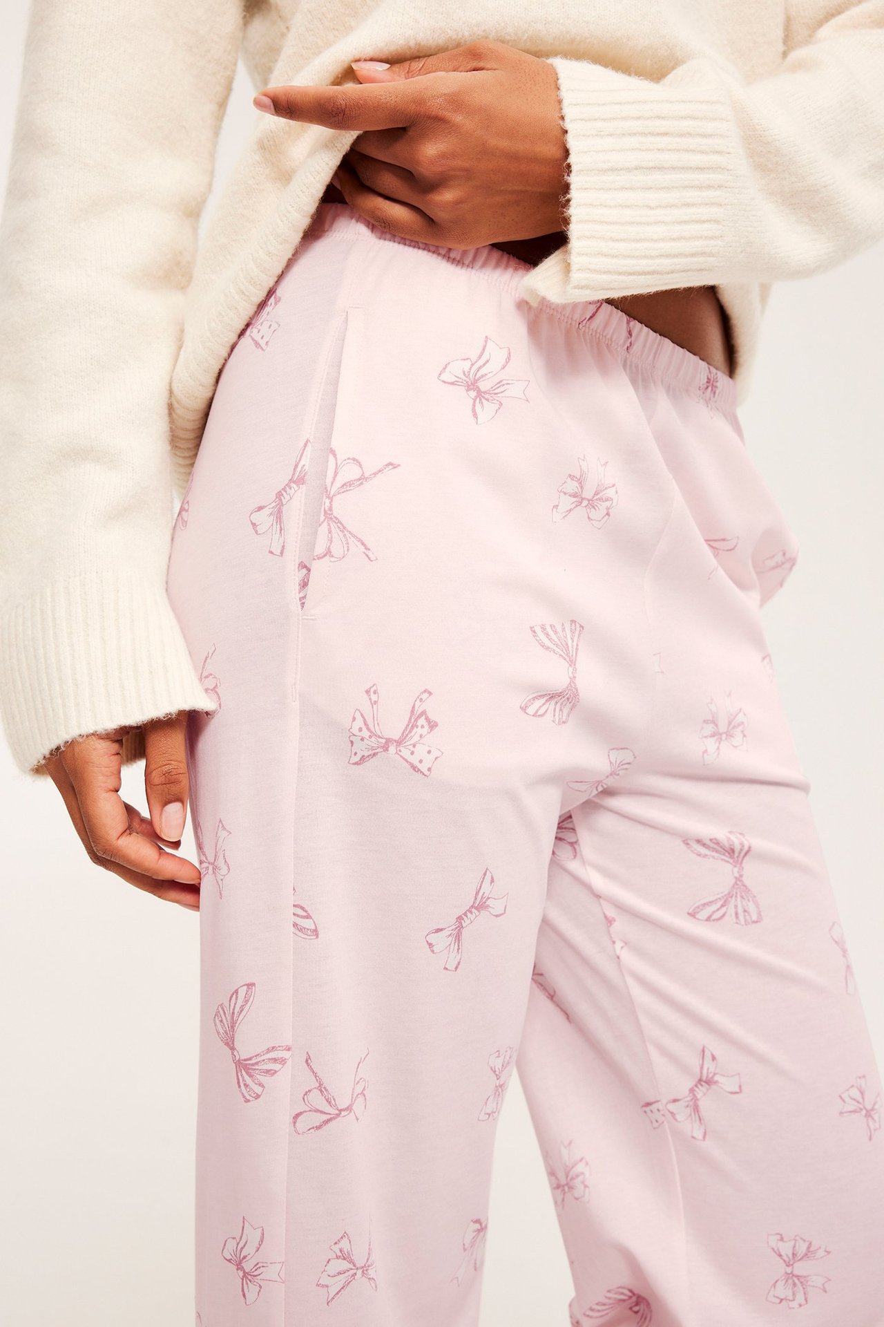 Nainen valkoisessa neuleessa ja vaaleanpunaisissa inkkarimuotoisissa pyjamahousuissa.