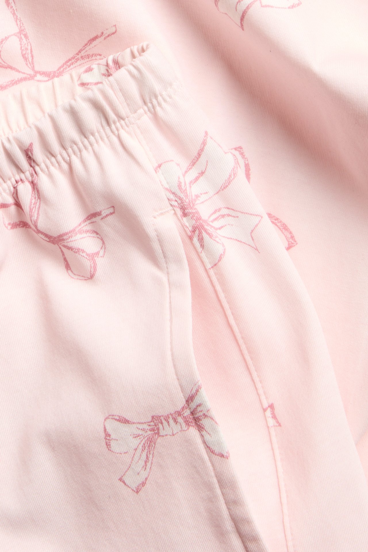 Närbild på rosa pyjamasbyxor i bomull med mörkt rosa rosettmönster, resår i midjan och sidficka.