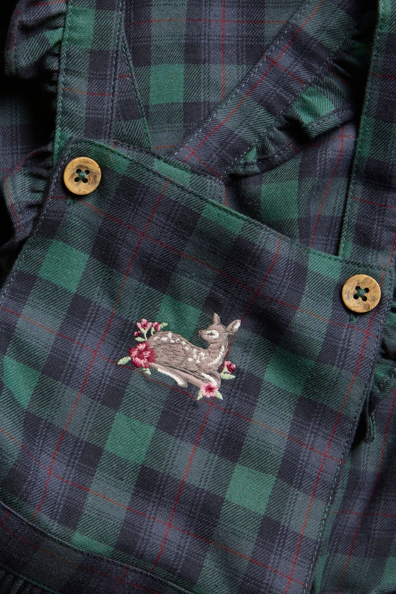 Zbliżenie na zielono-granatową sukienkę w kratę, z haftem sarenki i drewnianymi guzikami.