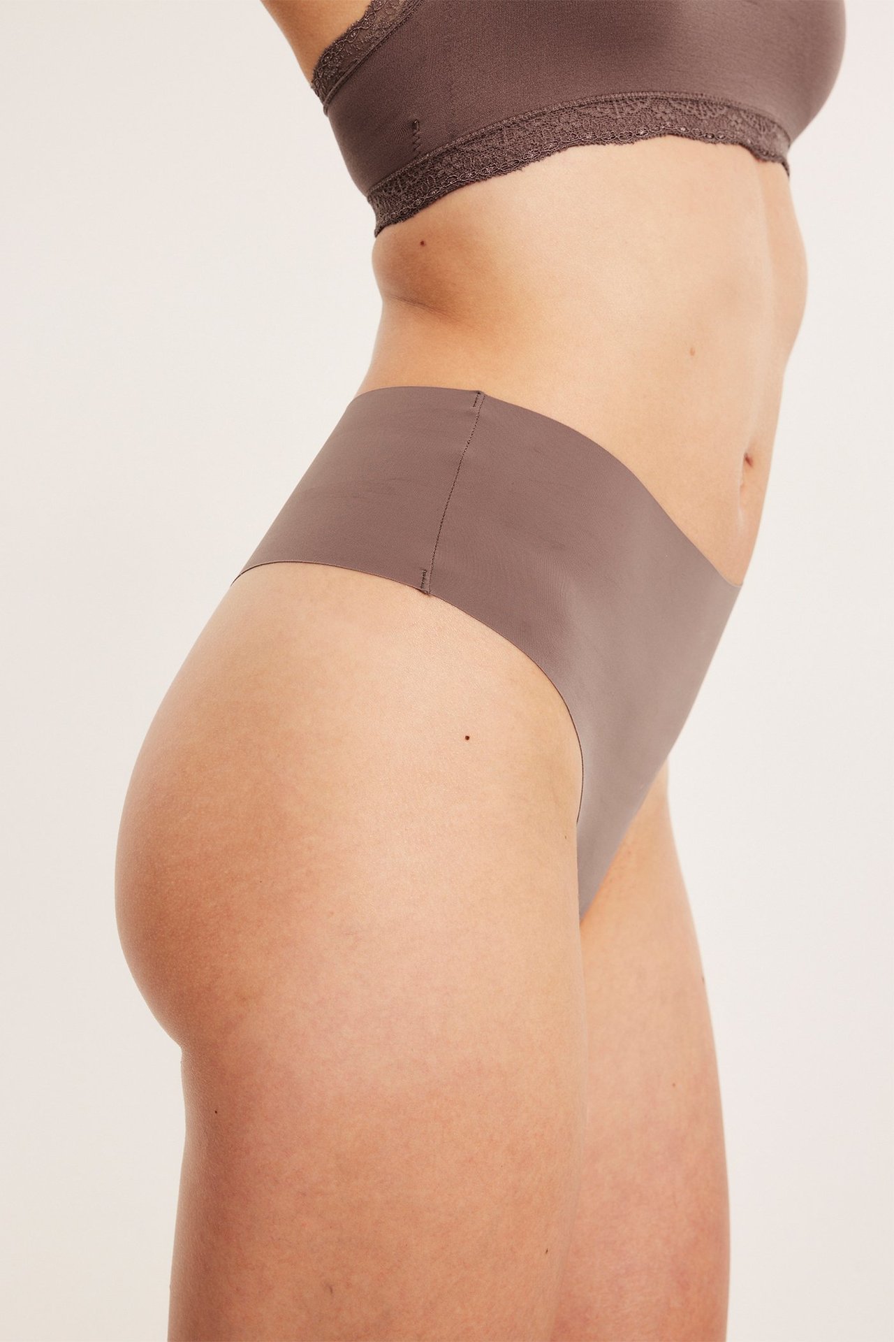 Naisen sivukuva tummanpinkissä saumattomassa stringissä ja yhteensopivassa pitsiliiveissä.