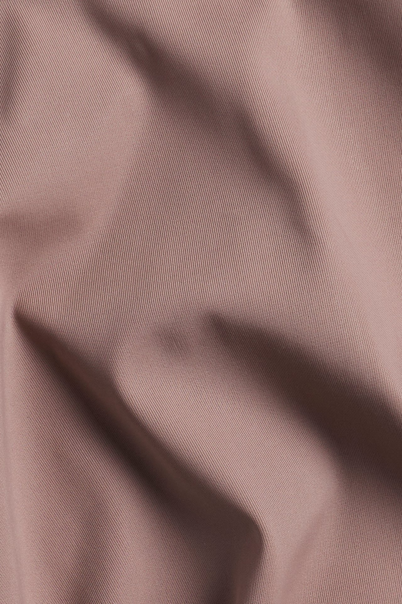 Zbliżenie ciemnoróżowego, jednolitego materiału stringów, ukazujące subtelną teksturę i miękkie fałdy.