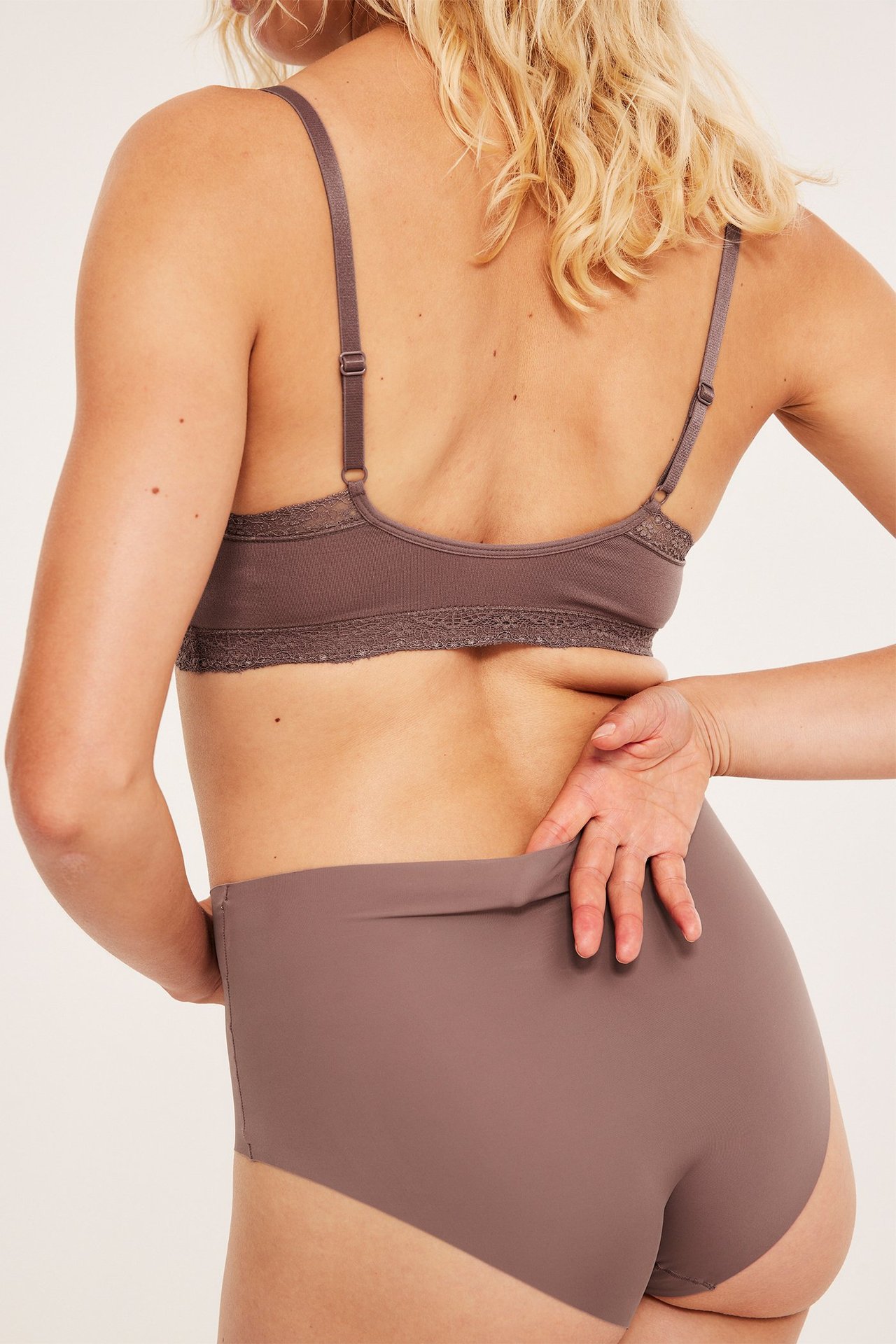 Ryggvisning av kvinne i mørk rosa sømløs hipster-truse og matchende blondekantet BH.