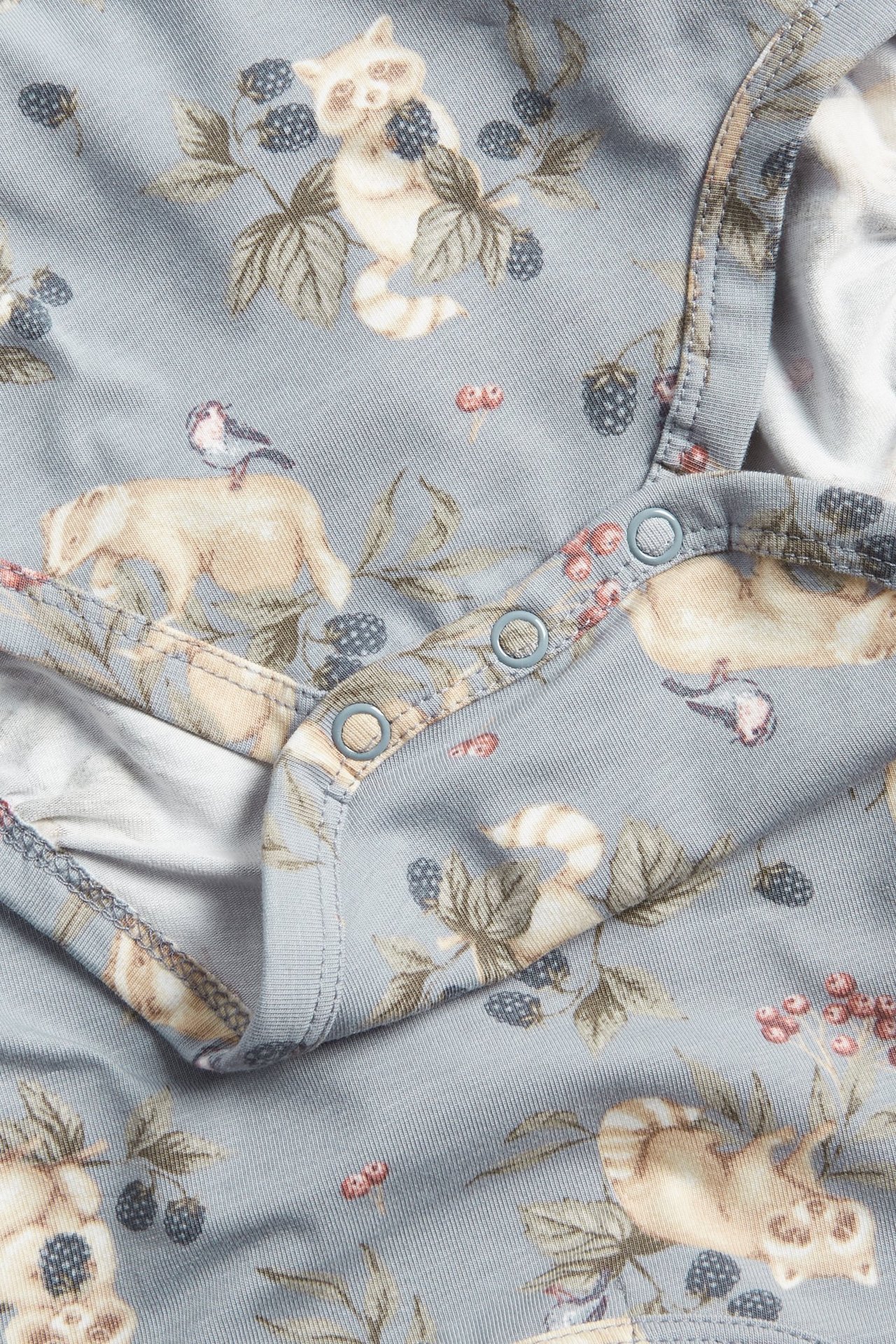 Zbliżenie na jasnoniebieskie body niemowlęce z wzorem zwierząt i jagód, z zatrzaskami.