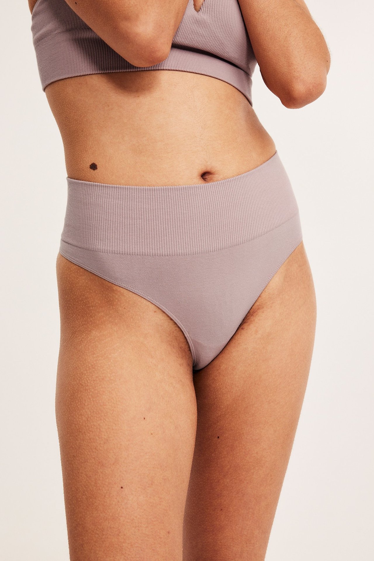 Nærbilde forfra av en kvinne i mauve rosa sømløse stringtruser med ribbet midje og matchende BH-topp.