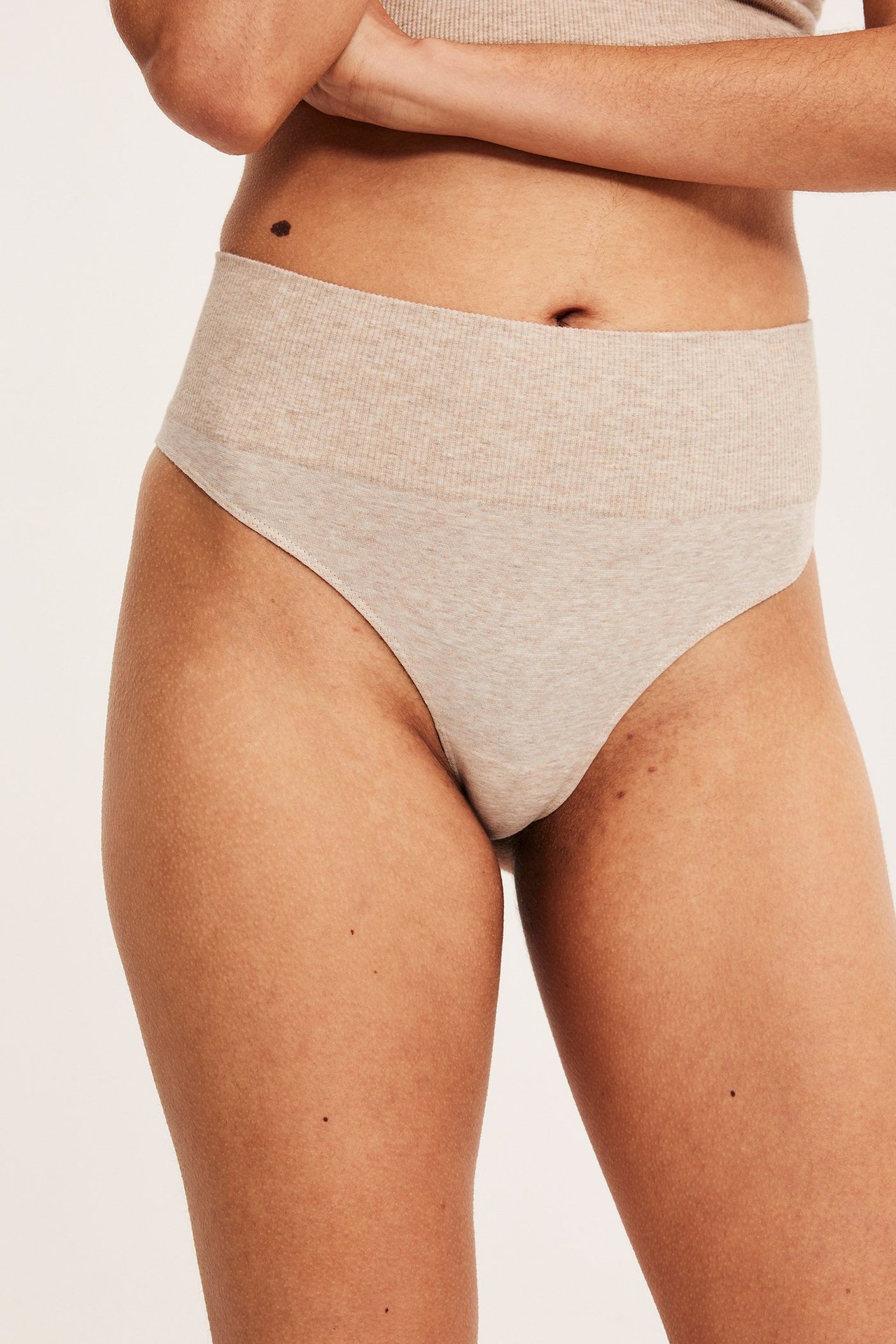 Frontvisning av kvinne i beige melert sømløs stringtruse med ribbet linning og matchende topp.