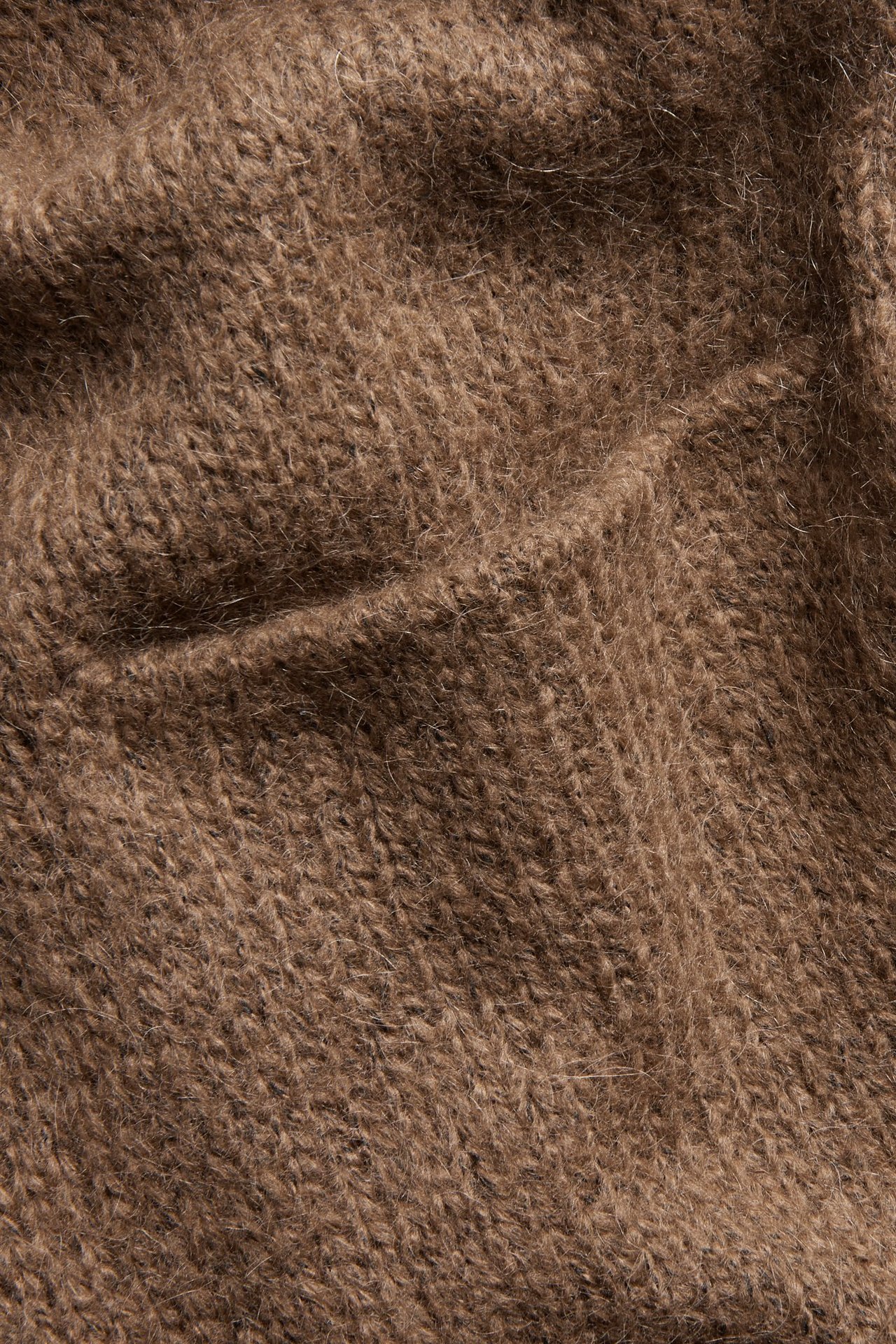 Zbliżenie na brązowy, puszysty materiał swetra z mieszanki wełny o widocznej dzianinowej fakturze.