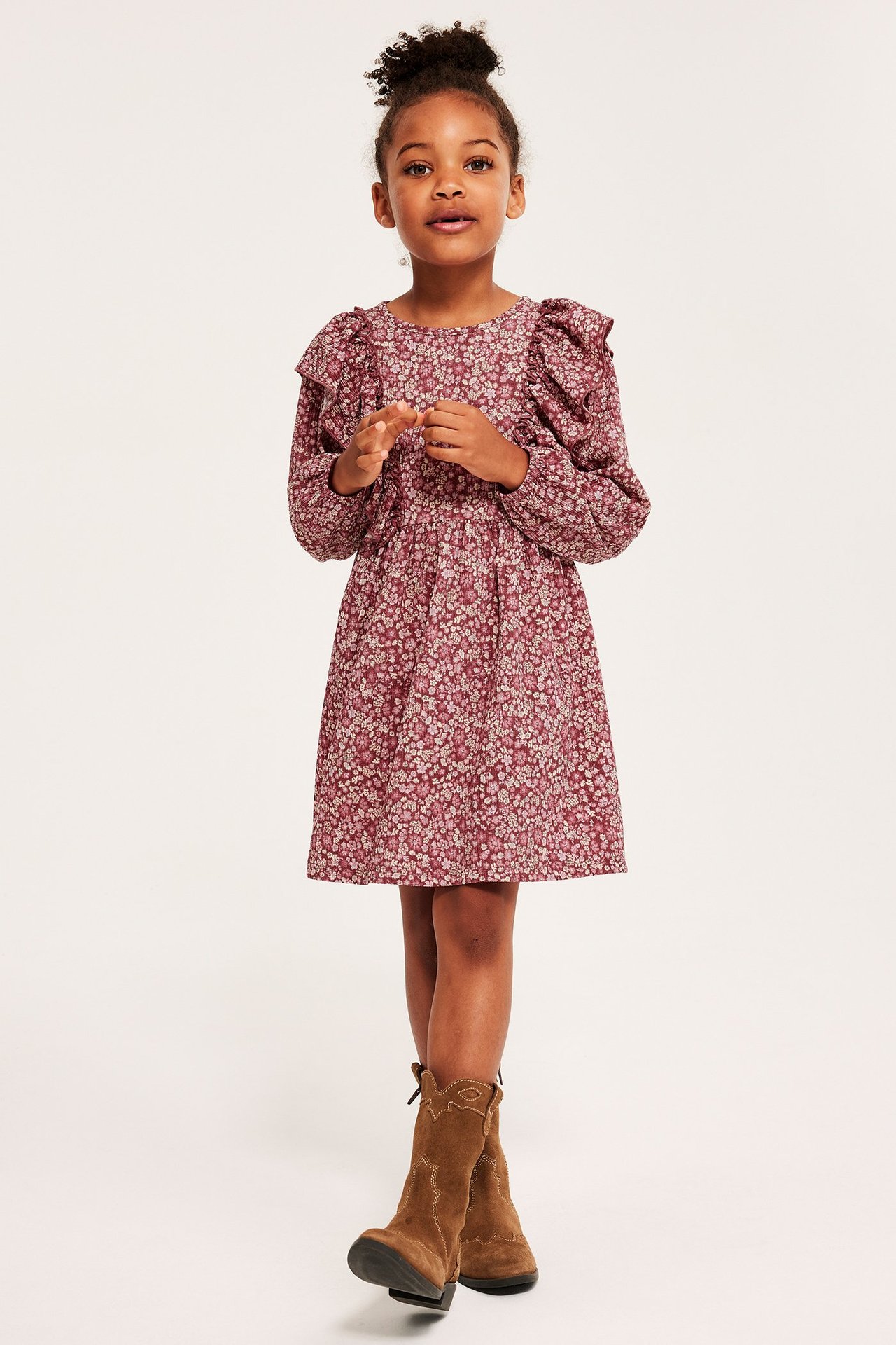 Frontvisning av barn i vinrød blomstret krepp-jerseykjole med rysjer på skuldrene og brune cowboystøvler.