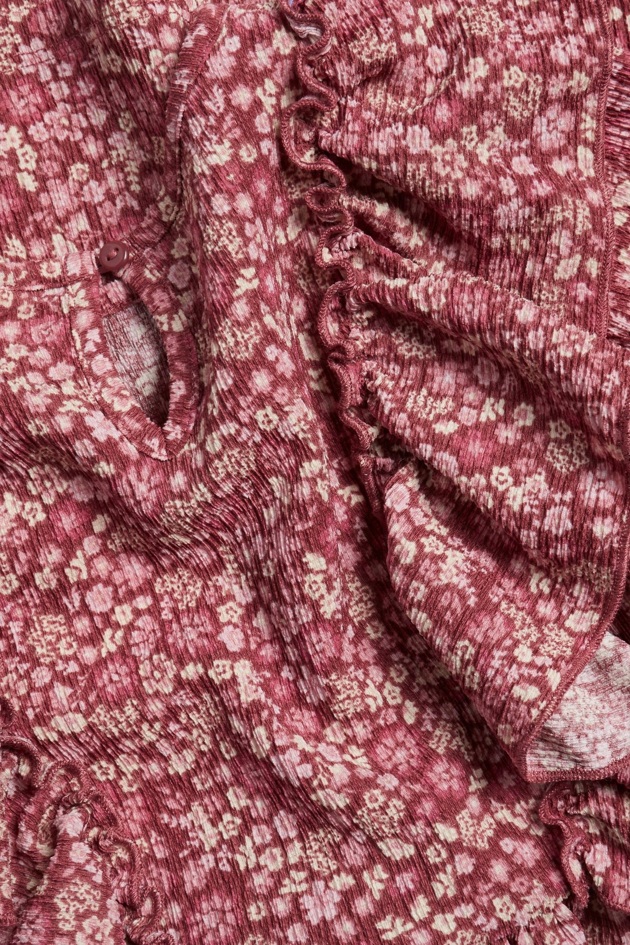 Zbliżenie na bordową sukienkę z krepowanej dzianiny w kwiatowy wzór, z falbankami i zapięciem na guzik.