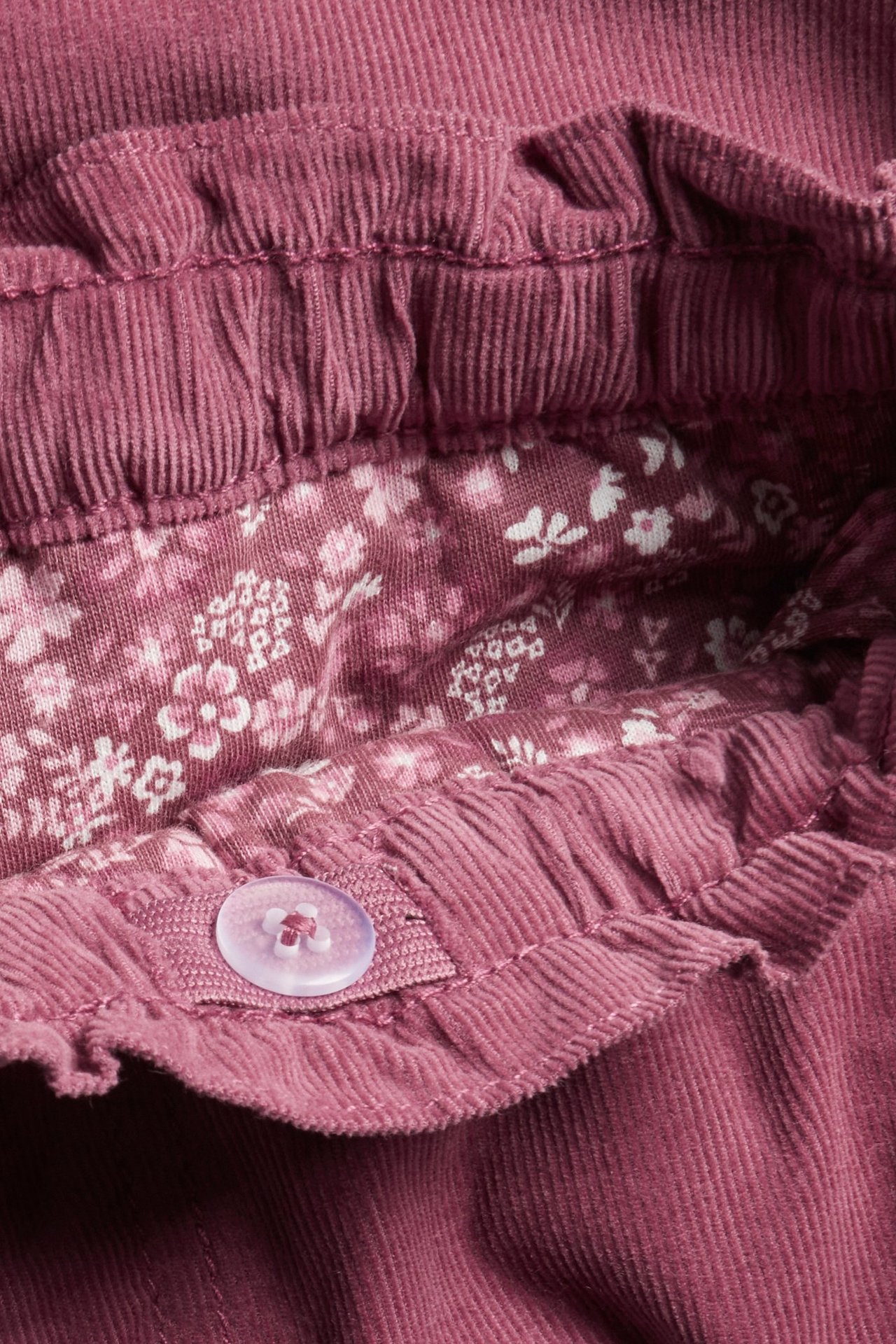 Zbliżenie na ciemnoróżowe sztruksowe spodnie dziecięce z regulowaną talią i bawełnianą podszewką w kwiaty.