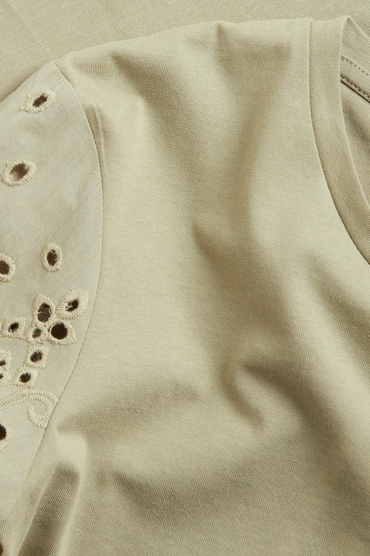Lähikuva vaaleanvihreästä puuvillaisesta T-paidasta, jossa broderie anglaise -hihat.