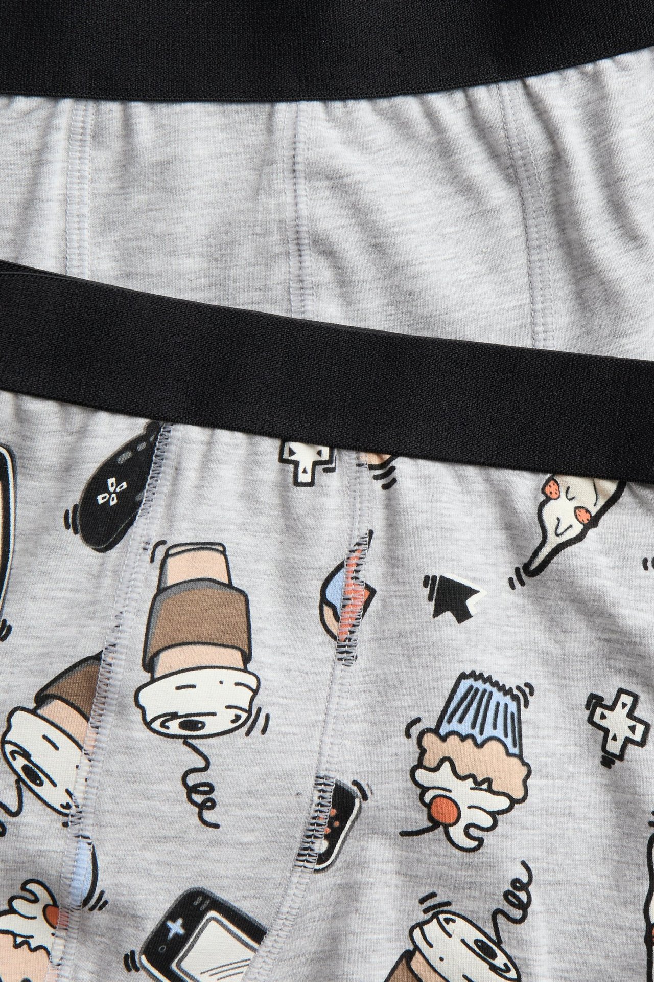 Zbliżenie na dwie szare melanżowe bokserki dziecięce, jedne gładkie, drugie z nadrukiem, obie z czarną gumką.