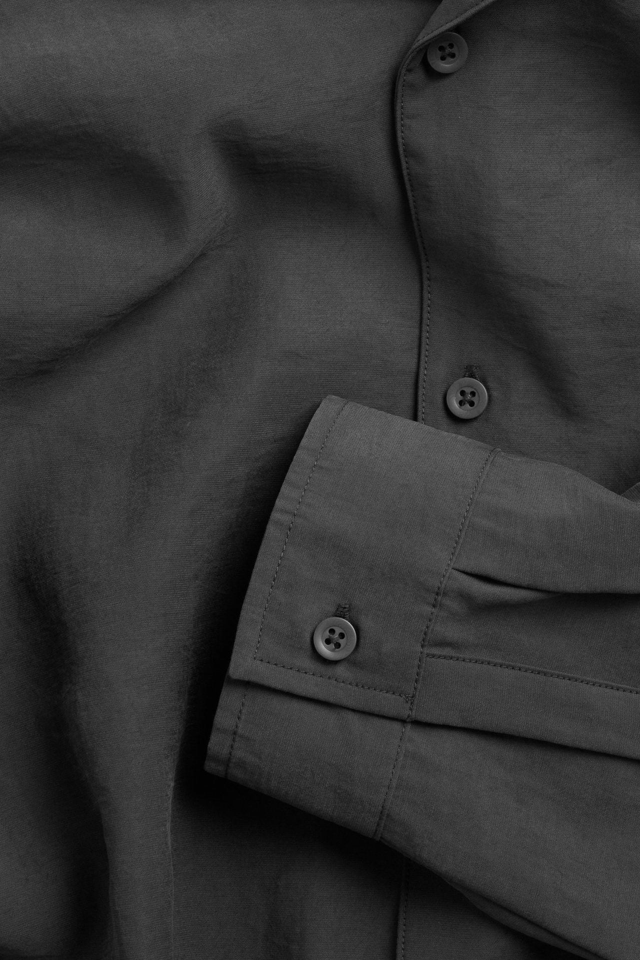 Nærbilde av en svart resortskjorte i modal/polyester med synlige knapper på knappestolpe og mansjett.