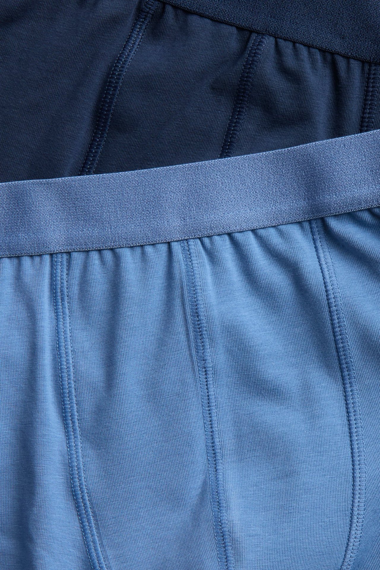 Zbliżenie na jasnoniebieskie jednolite bawełniane bokserki z pasującą gumką w pasie oraz ciemnoniebieskie bokserki.