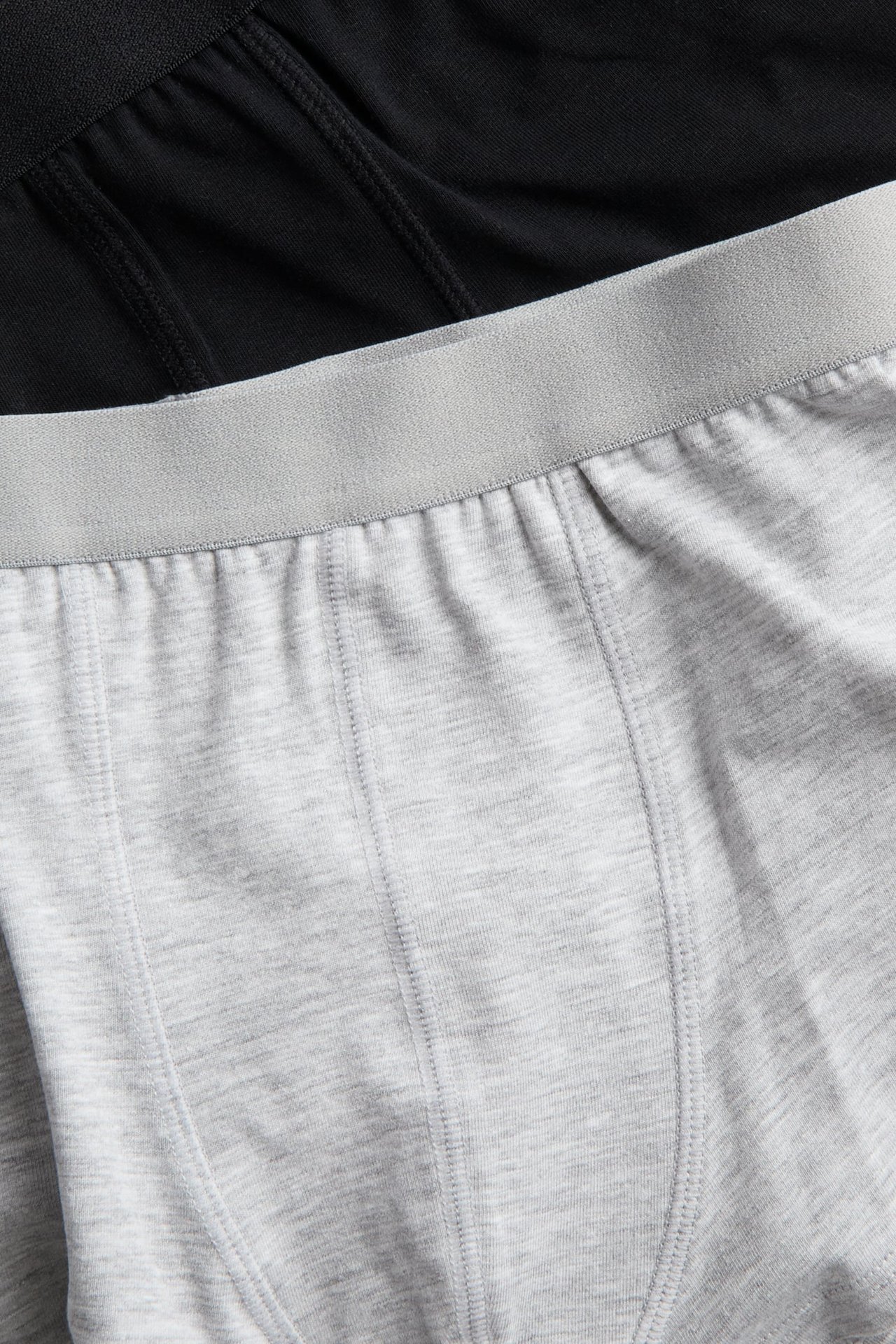 Nærbilde: lyse gråmelerte boksershorts i bomullsmix med grå strikklinning, pluss svarte boksershorts bak.