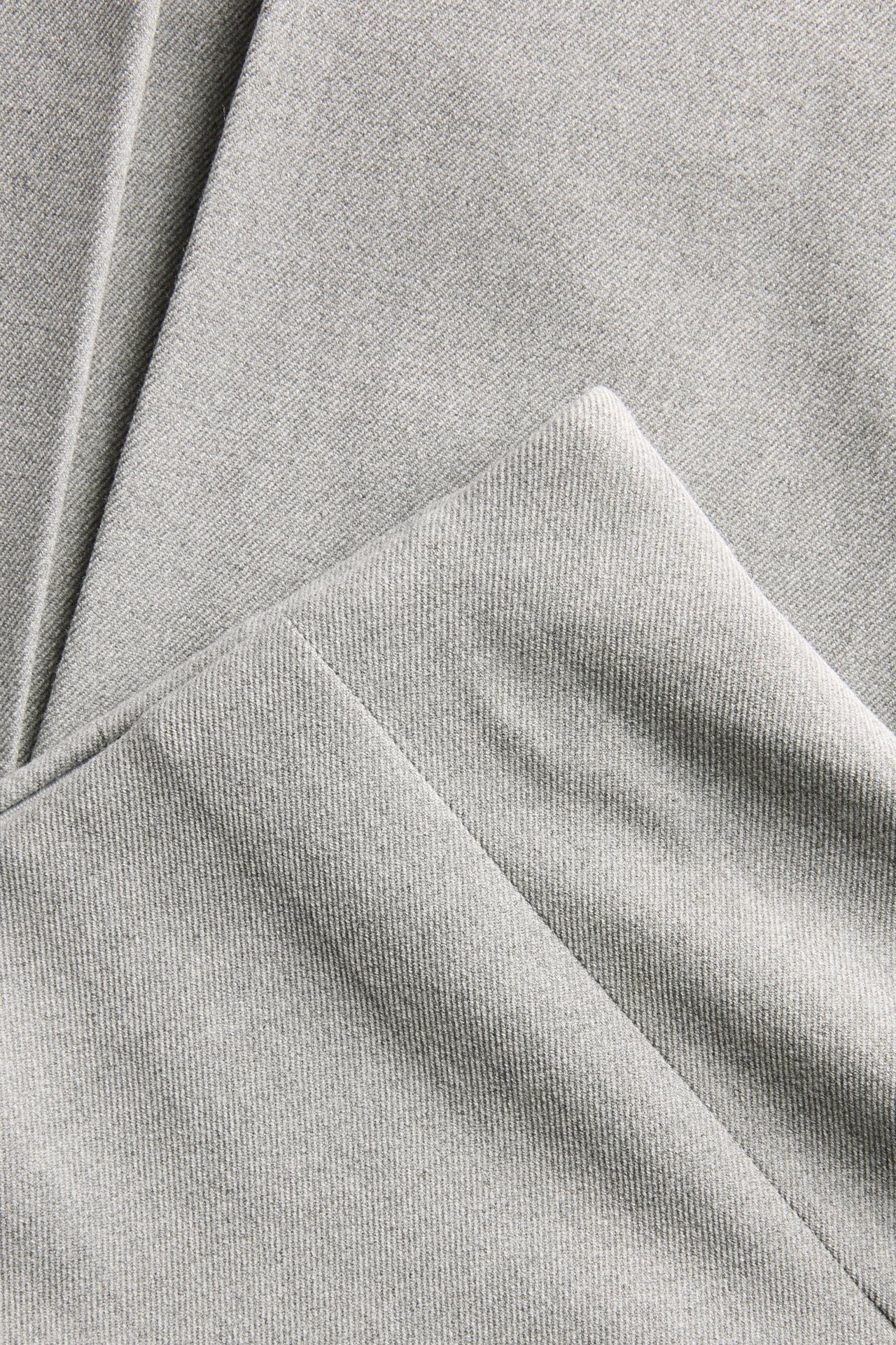 Zbliżenie jasnoszarej melanżowej plisowanej spódnicy, ukazujące fakturę materiału.