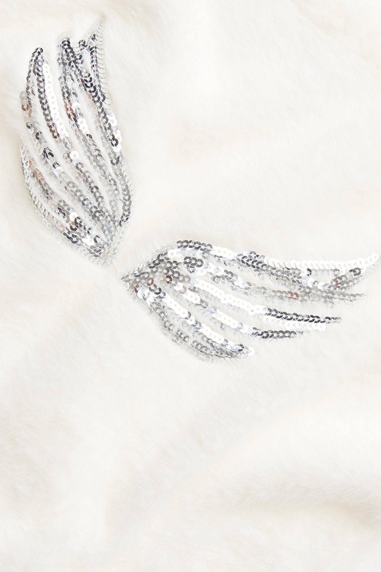 Zbliżenie na kremowy dzianinowy top z przędzy piórkowej ze srebrnymi aplikacjami skrzydeł z cekinów.