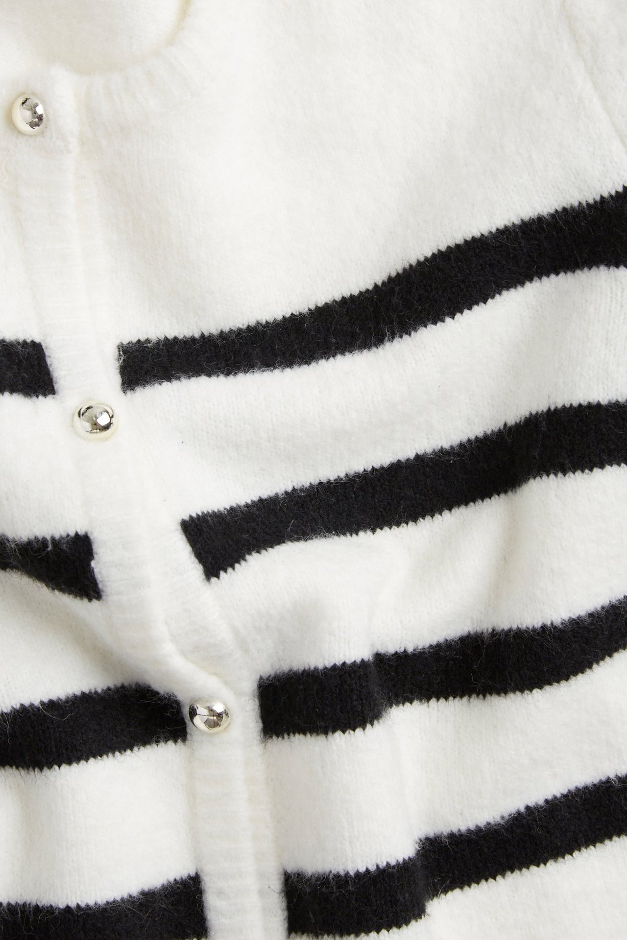Zbliżenie na kremowy i czarno-paskowany sweter rozpinany z ozdobnymi srebrnymi guzikami.