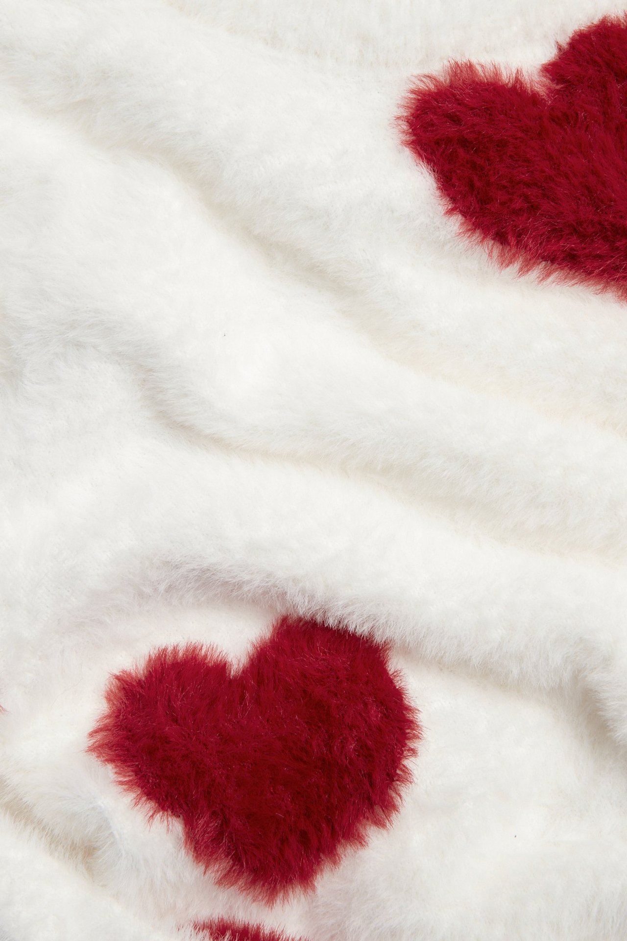 Zbliżenie na miękki, off-white sweter z pierzastej przędzy z czerwonymi sercami żakardowymi.