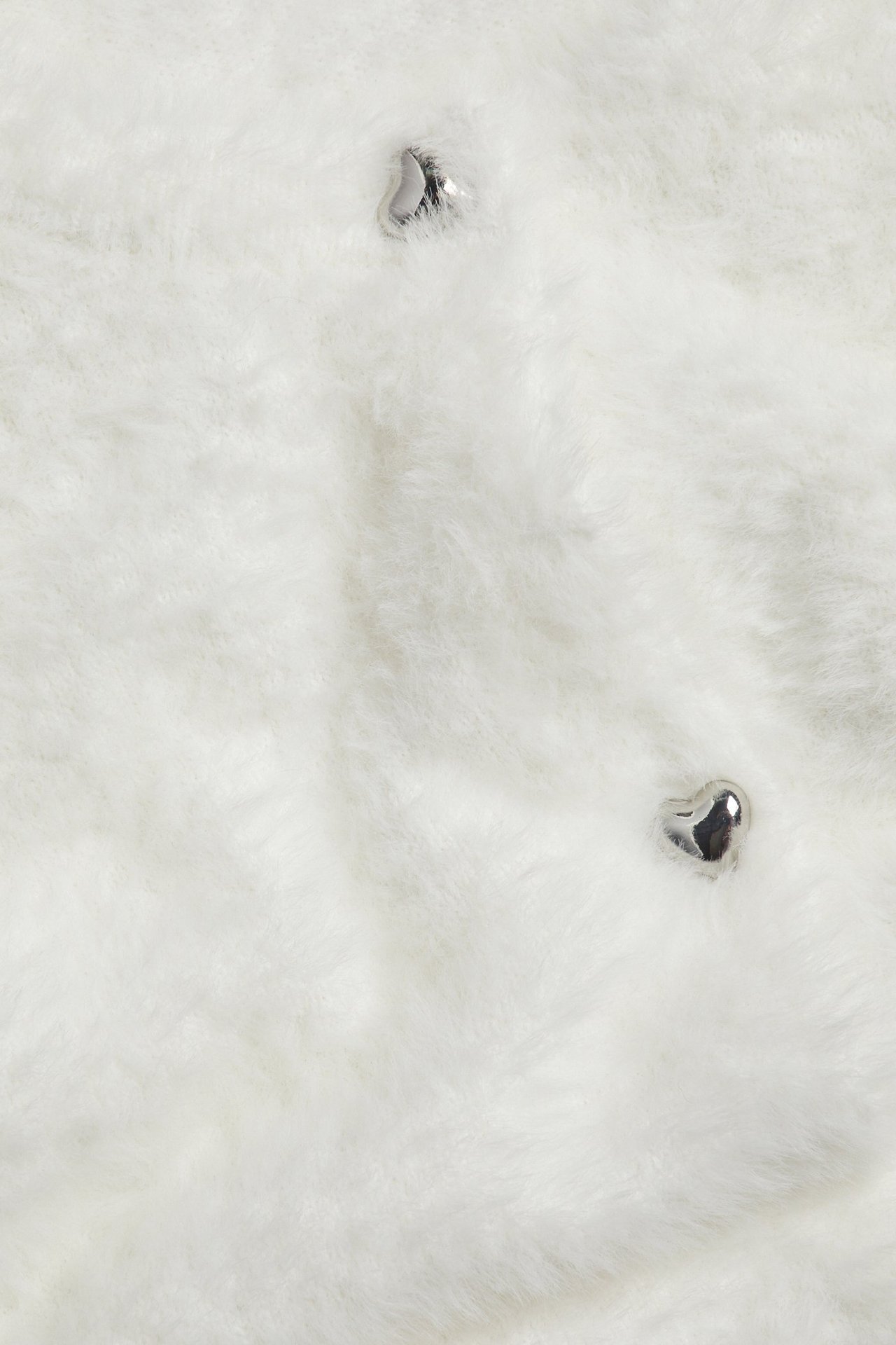 Zbliżenie kremowego swetra z przędzy piórkowej z dwoma srebrnymi guzikami w kształcie serca.