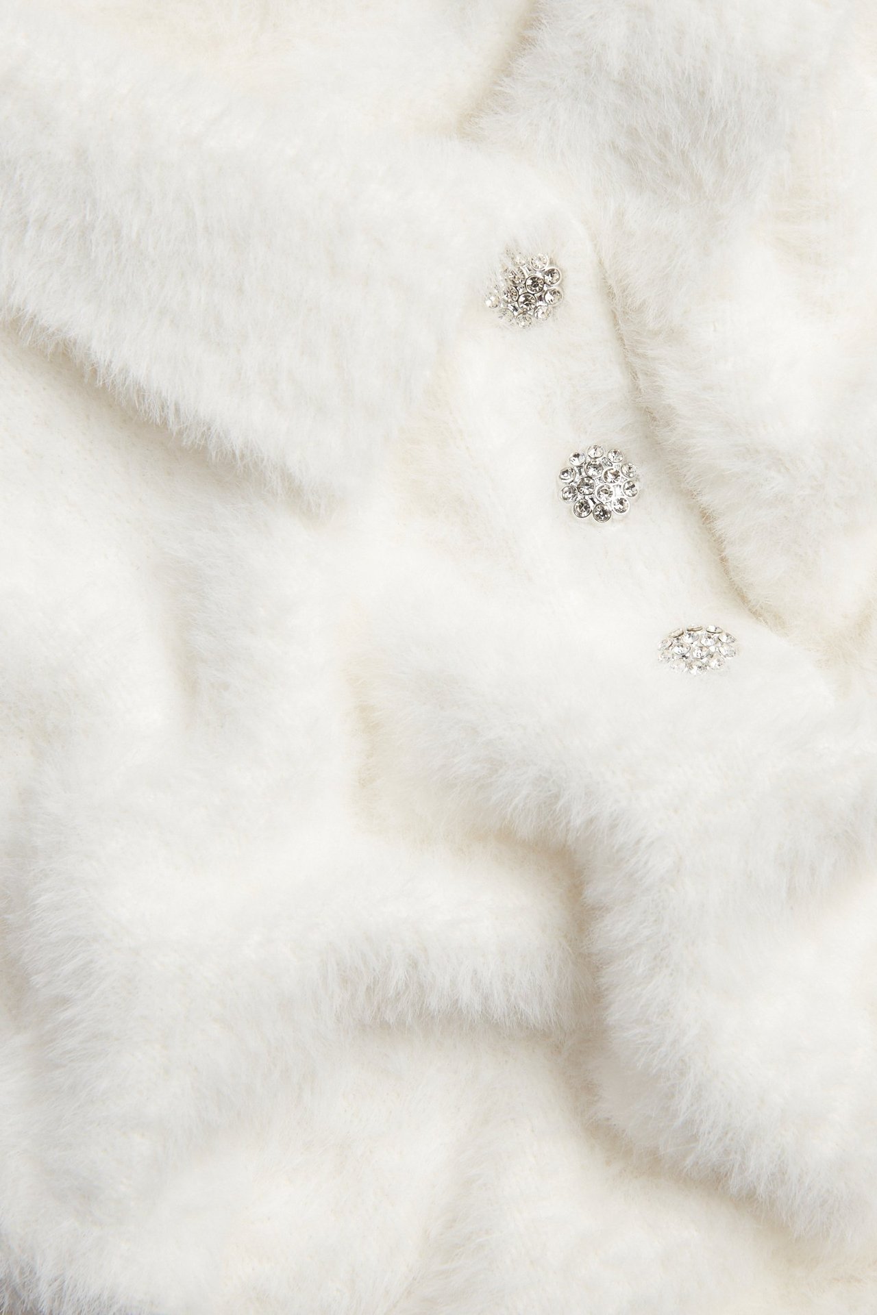 Zbliżenie na kremowy sweter z dzianiny z puszystej przędzy z kołnierzem i trzema ozdobnymi guzikami.