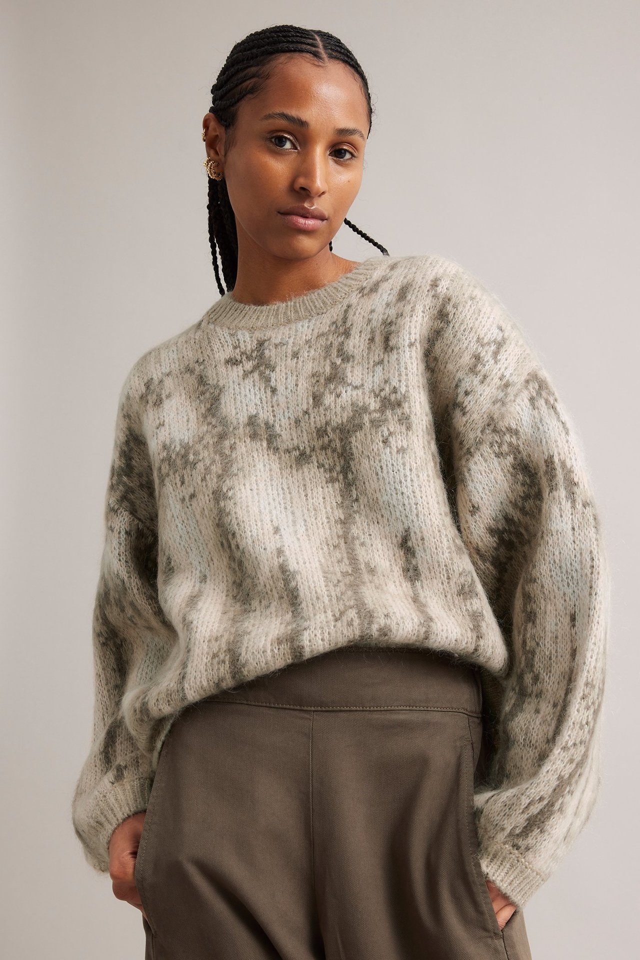 Edestä: nainen yllään rento beige ja ruskea jacquard-kuvioinen villasekoitusneule ja tummanruskeat housut.