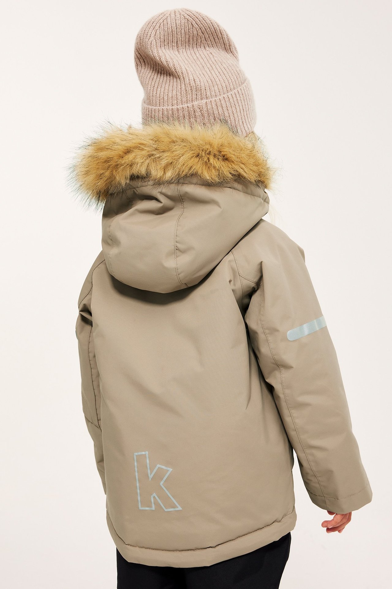 Widok z tyłu: dziecko w beżowej kurtce zimowej z kapturem obszytym futrem i jasnobeżowej czapce.