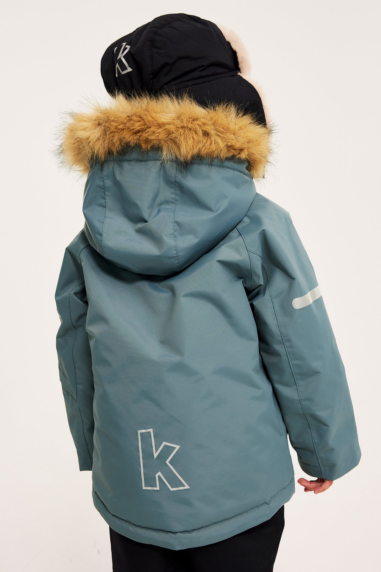 Widok z tyłu dziecka w niebieskiej kurtce zimowej z kapturem z brązowym futrem i czarną czapką.