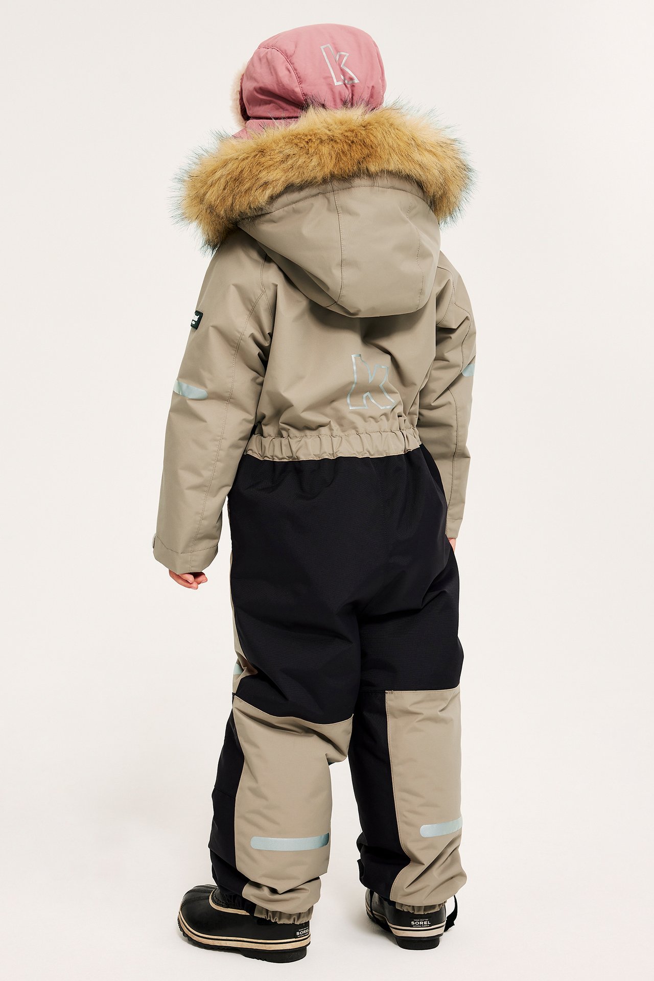 Widok z tyłu: dziecko w beżowo-czarnym kombinezonie zimowym z kapturem obszytym futrem i czarnych butach.