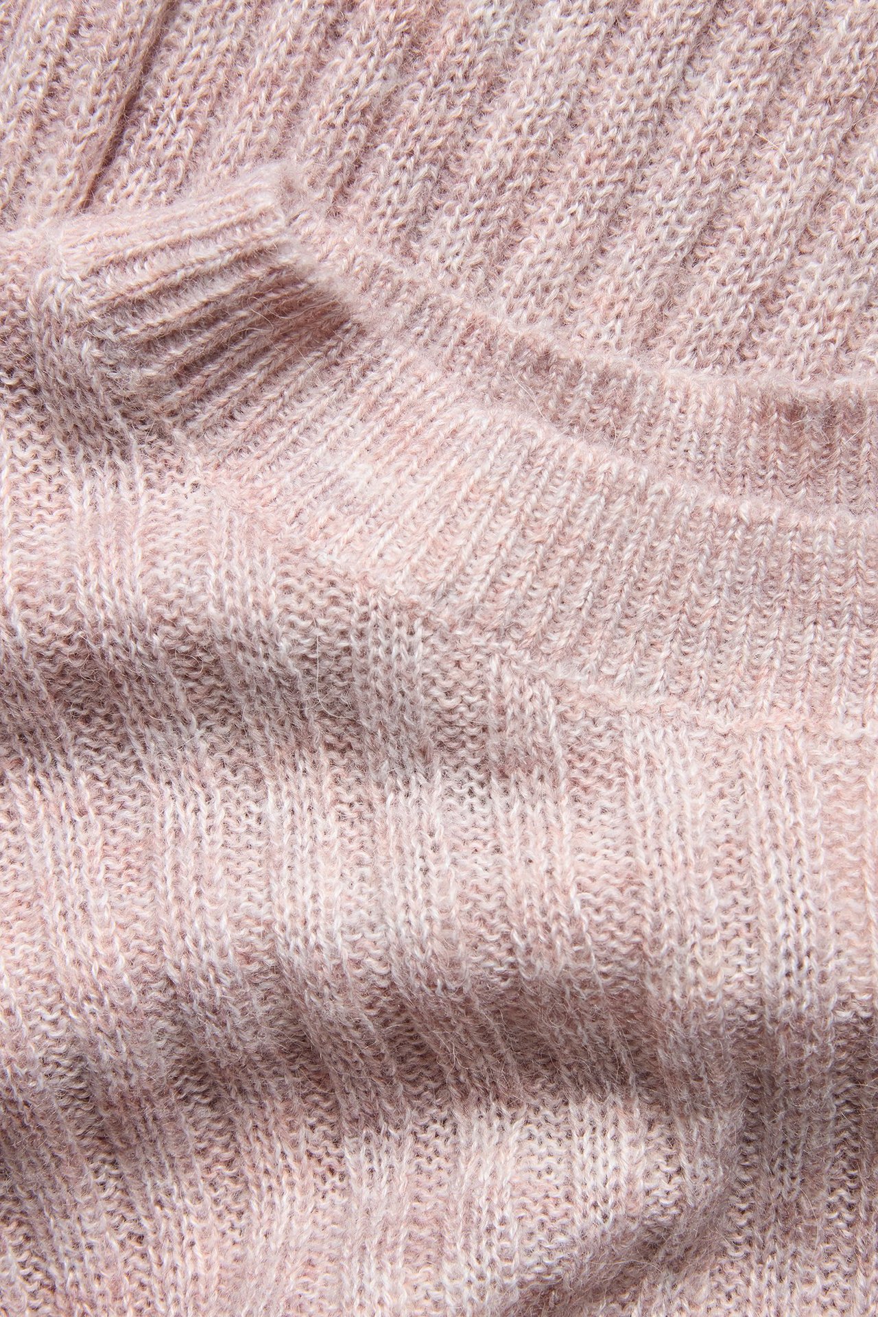 Lähikuva vaaleanpunaisesta meleeratusta ribbineuleisesta lyhythihaisesta neuleesta, jossa on pörröinen pinta.