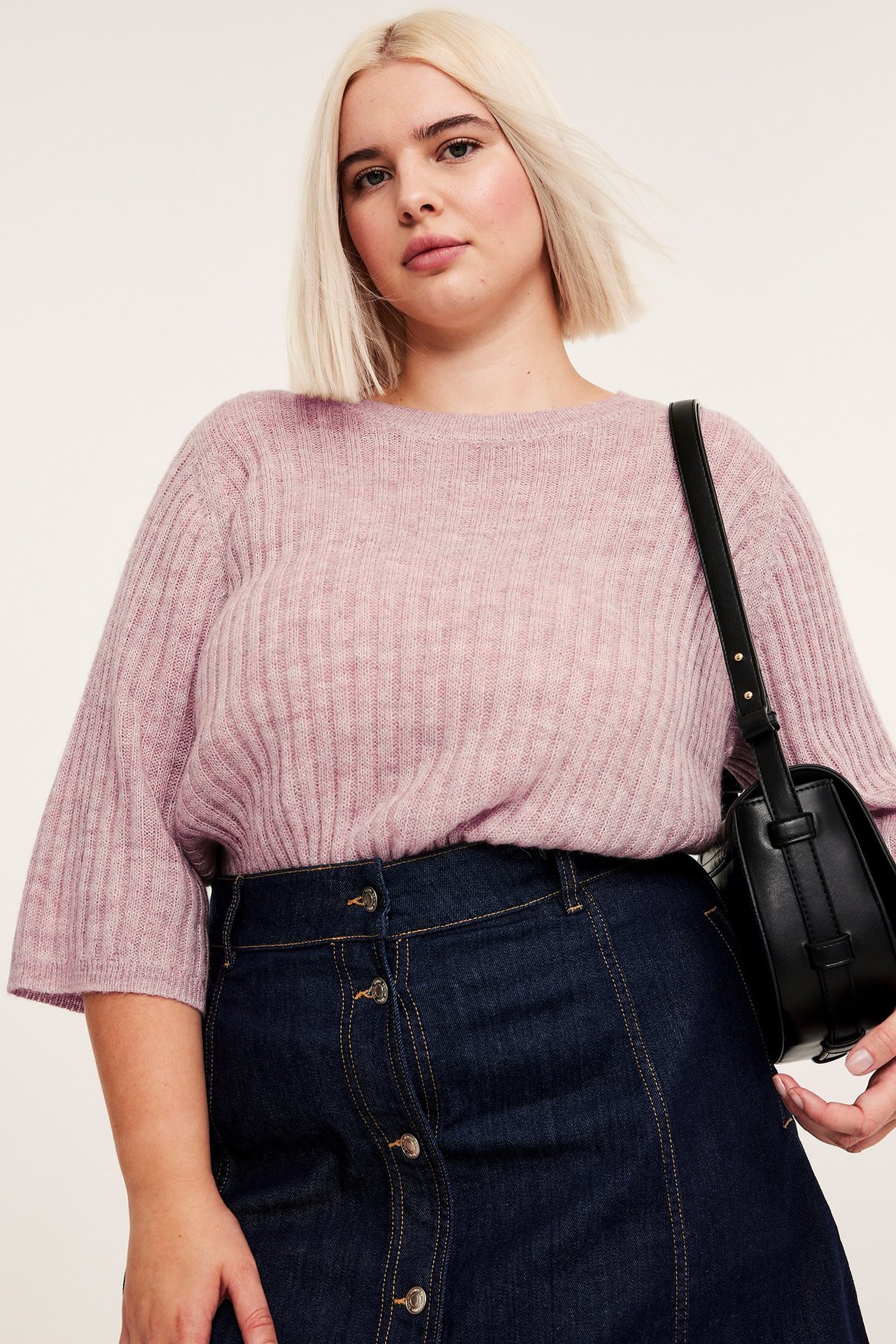 Edestä: nainen vaaleanpunaisessa ribbineuleessa lyhyillä hihoilla, tummansinisessä farkkuhameessa, musta käsilaukku.