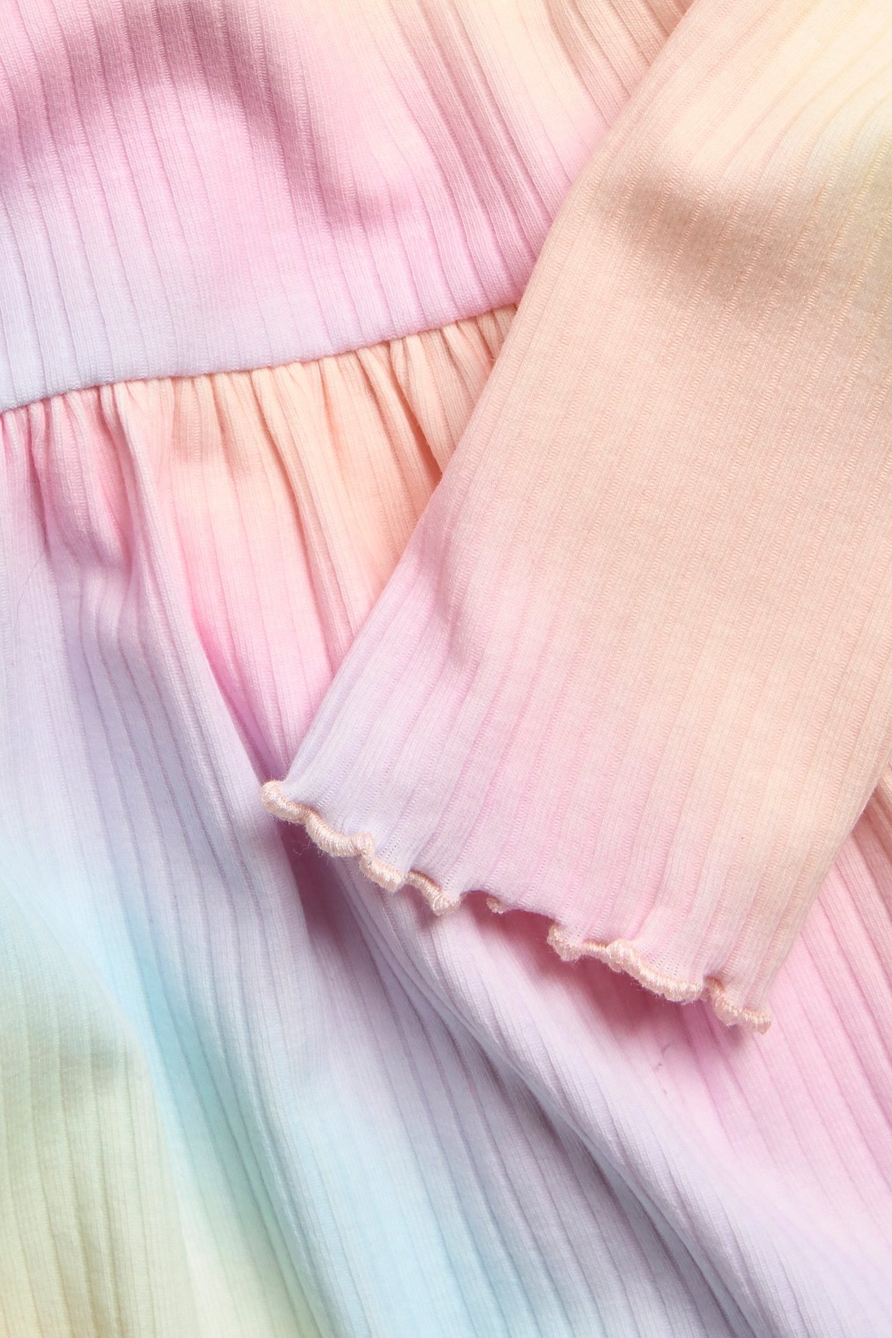 Zbliżenie na dziecięcy prążkowany tęczowy top peplum z marszczoną talią i falbankowymi mankietami.