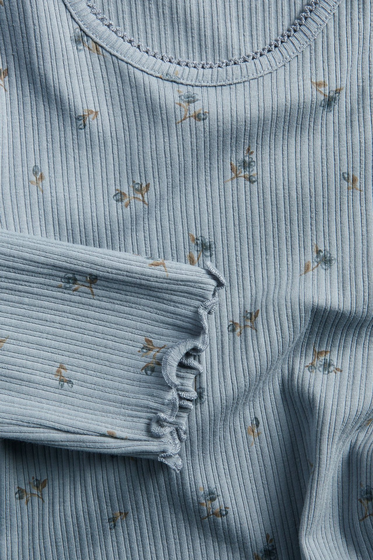 Zbliżenie jasnoniebieskiego prążkowanego topu niemowlęcego z długim rękawem, kwiatowym wzorem i wykończeniem picot.