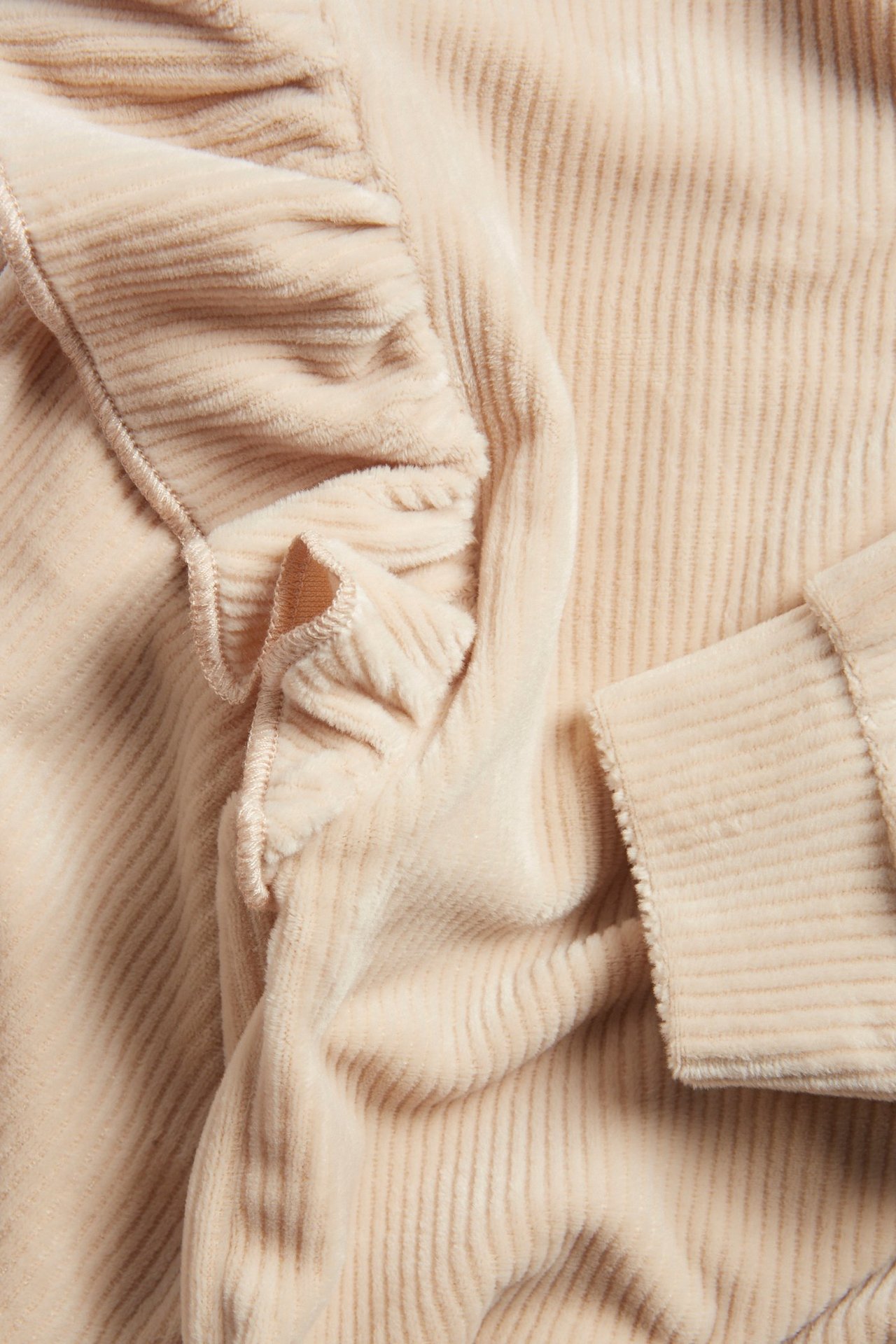 Zbliżenie beżowej prążkowanej welurowej bluzy z falbanką.