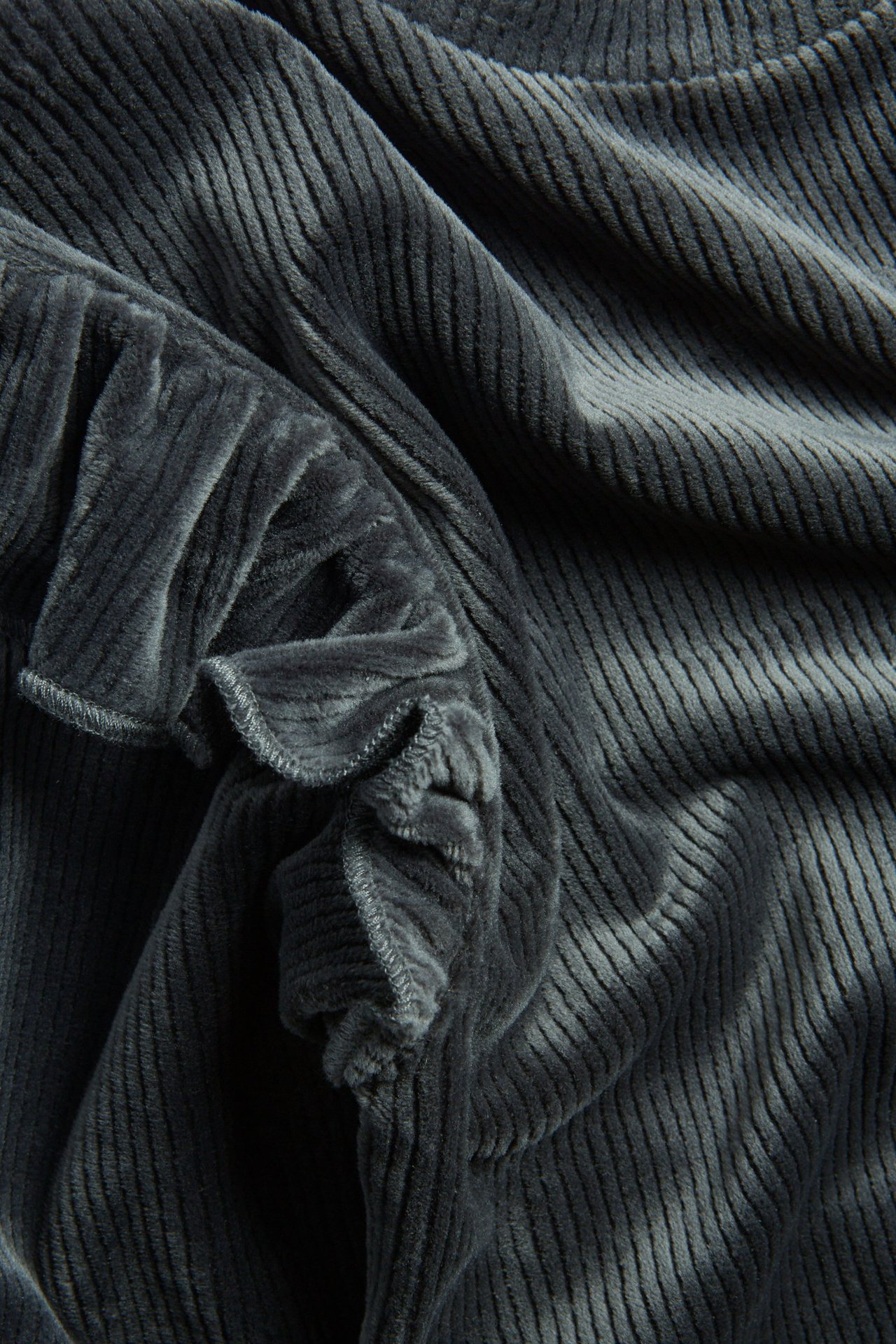 Zbliżenie na czarną prążkowaną bluzę welurową z falbanką.