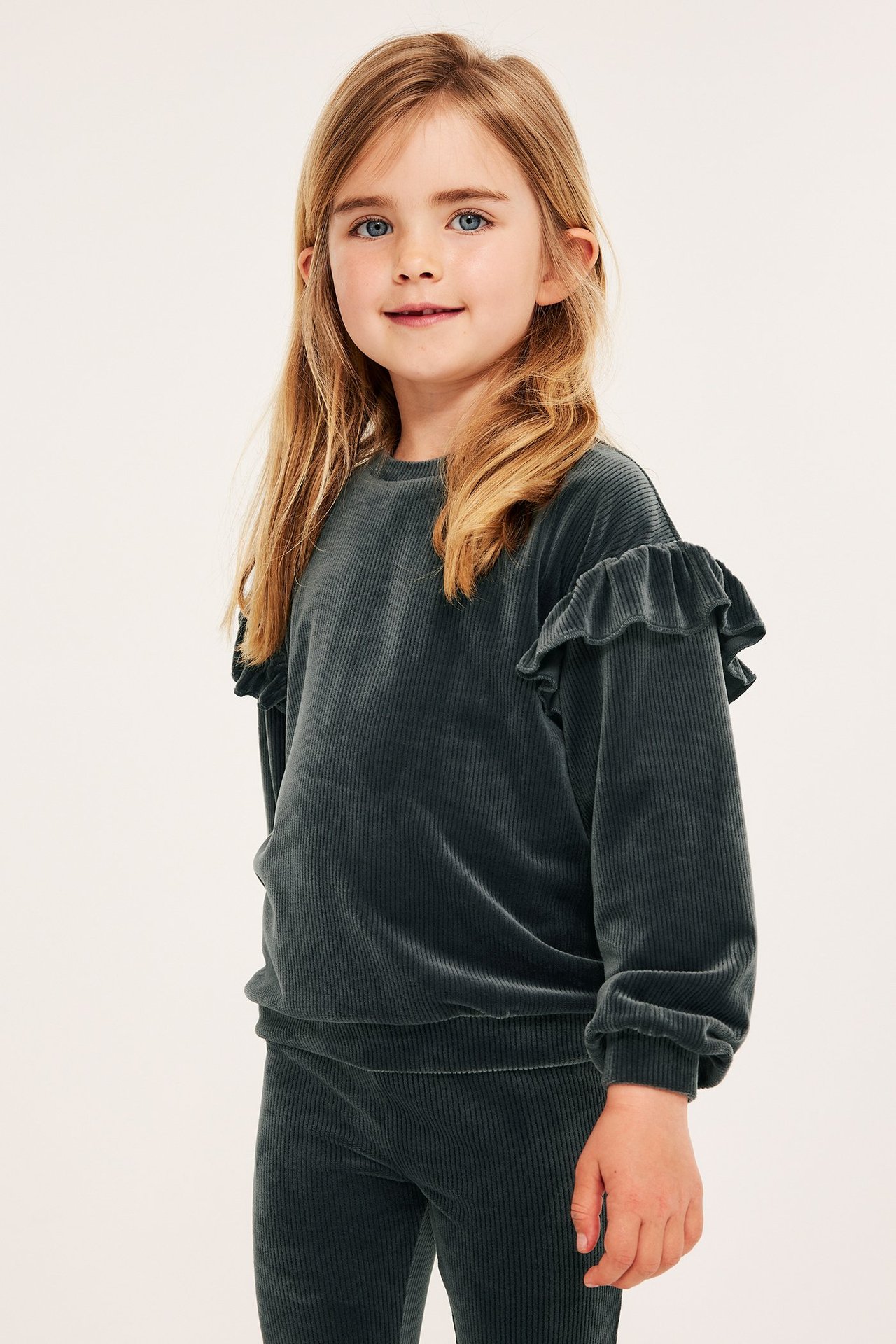Widok z przodu: dziecko w czarnej prążkowanej welurowej bluzie z falbankami i pasujących welurowych legginsach.