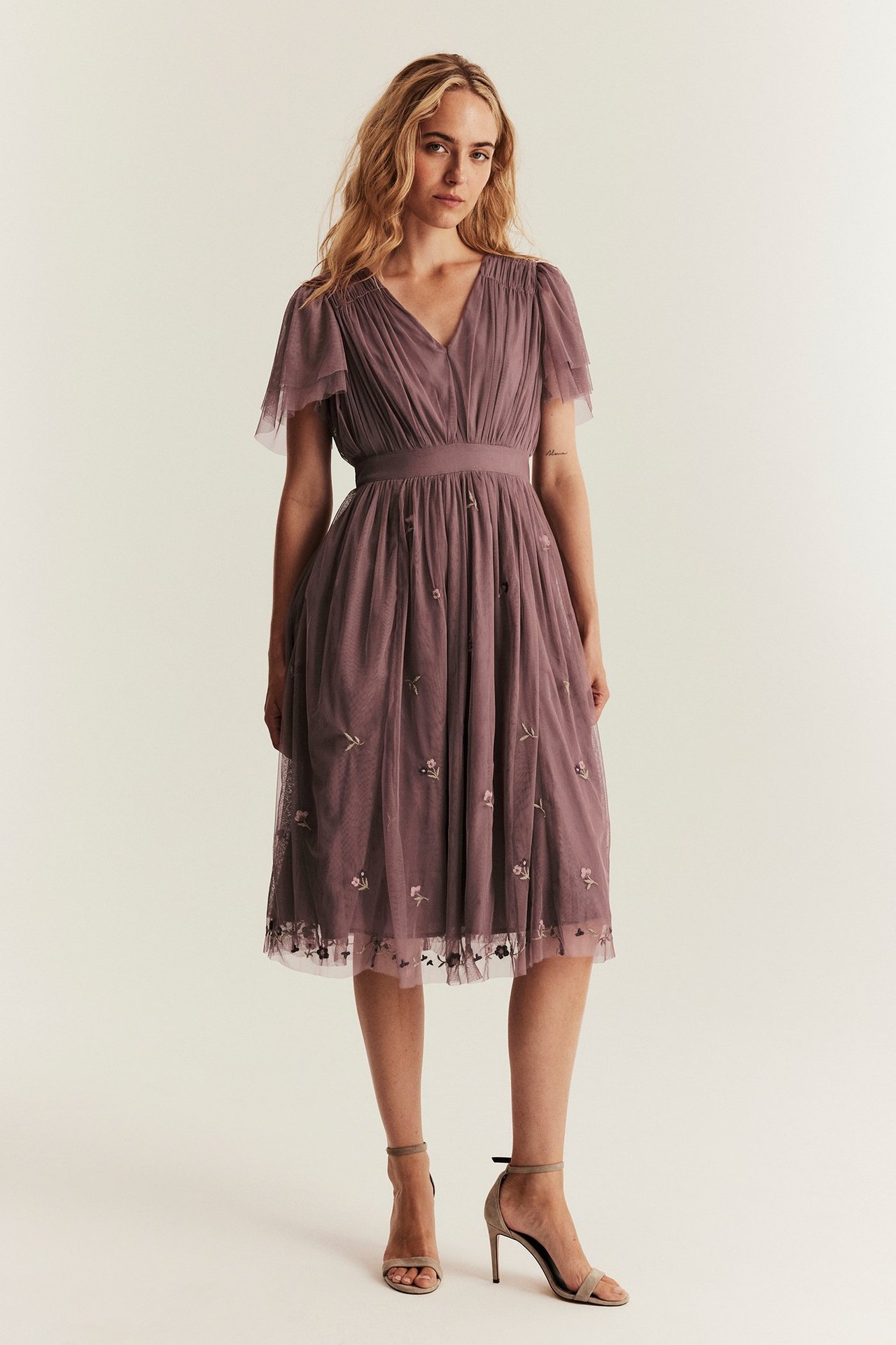 Etunäkymä, nainen pölyisen ruusunvärisessä mesh-mekossa, jossa V-kaula-aukko, liehuvat hihat ja kukkakirjonta.