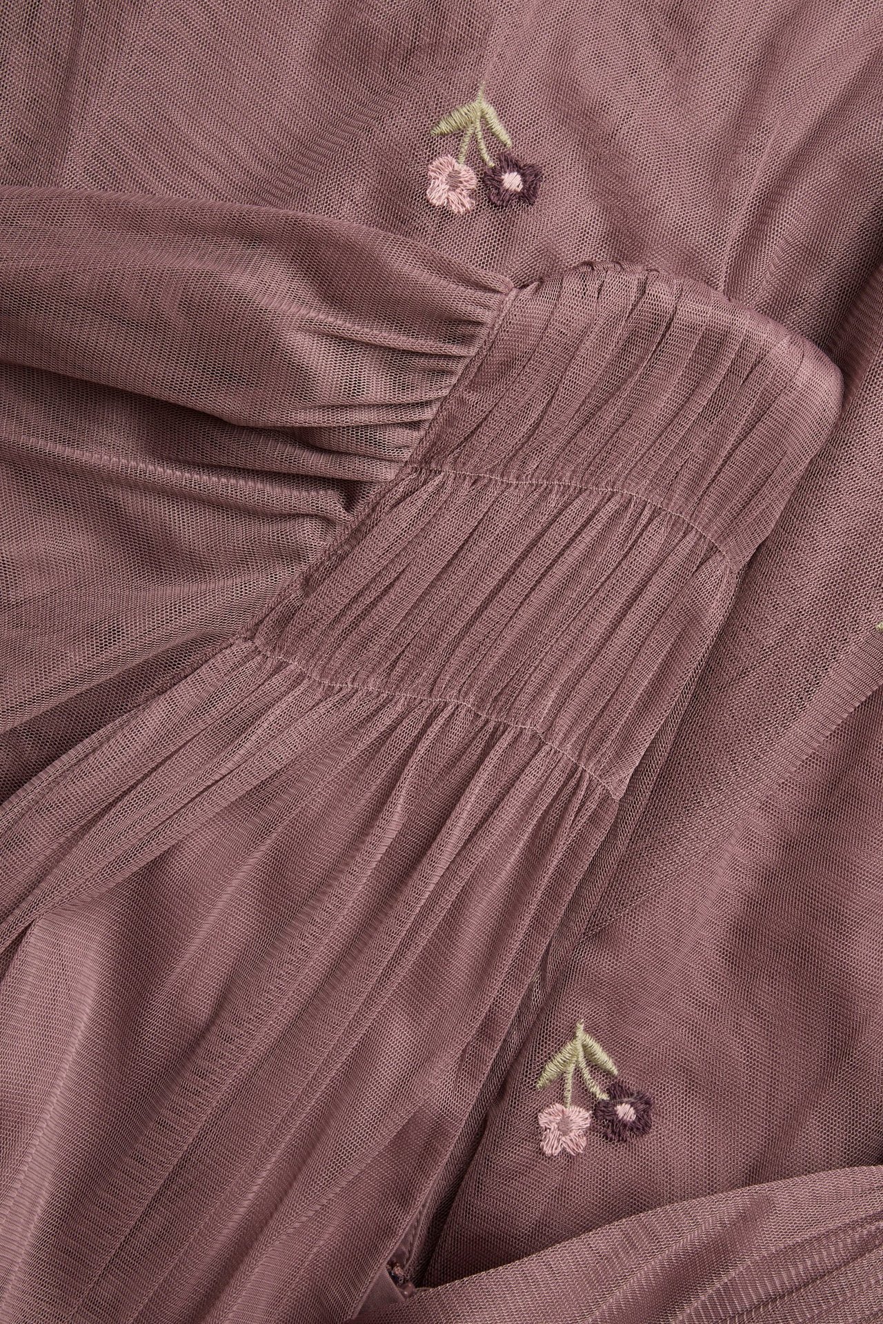 Nærbilde av en mørk rosa meshkjole med rynkede detaljer og brodert kirsebærmønster.