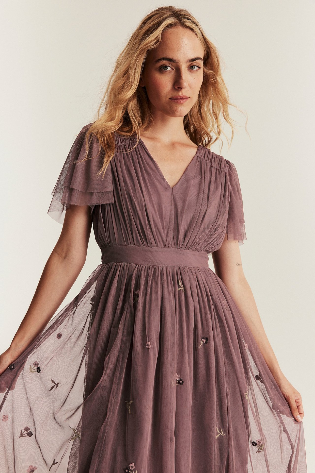 Widok z przodu: kobieta w ciemnoróżowej sukience z siateczki z falbankami i haftem kwiatowym.