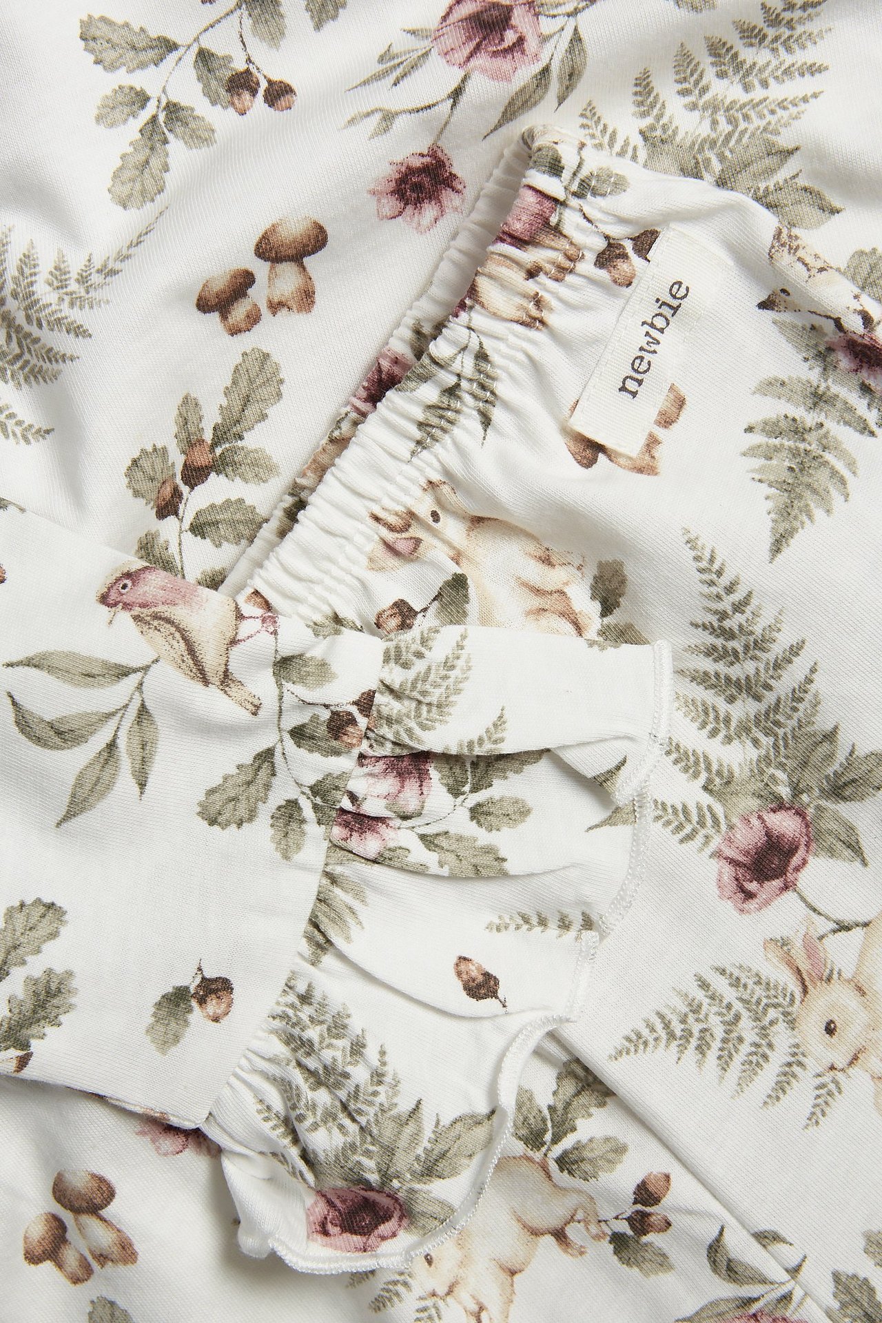 Zbliżenie na ecru bawełnianą piżamę dziecięcą z kwiatowym i leśnym wzorem, falbankami, elastyczną talią.