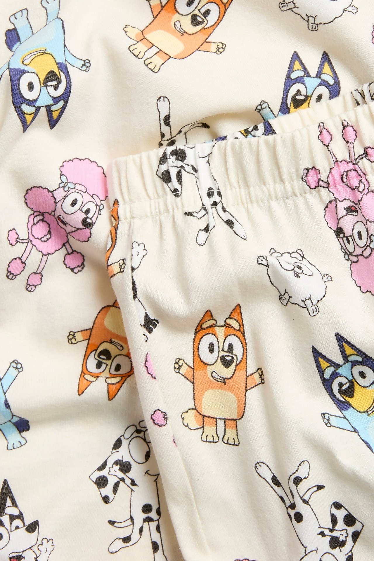 Zbliżenie na ecru bawełnianą piżamę dziecięcą z nadrukiem postaci Bluey i elastycznym pasem.