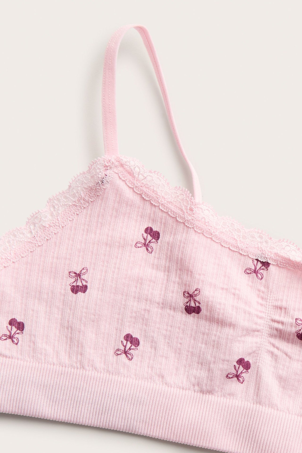 Zbliżenie różowego prążkowanego topu dziecięcego z cienkimi ramiączkami, koronką i wzorem w wiśnie.