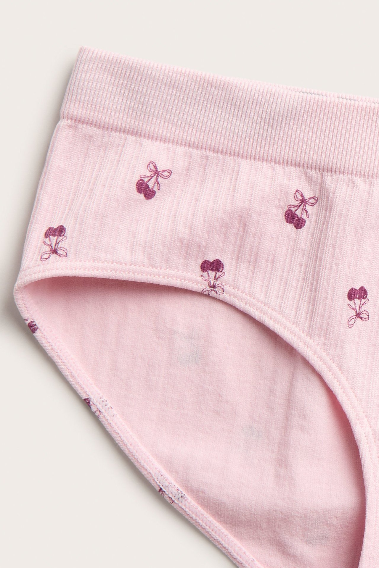 Lähikuva vaaleanpunaisista lasten hipster-alushousuista, joissa on kirsikkanauhakuvio ja ribattu vyötärönauha.