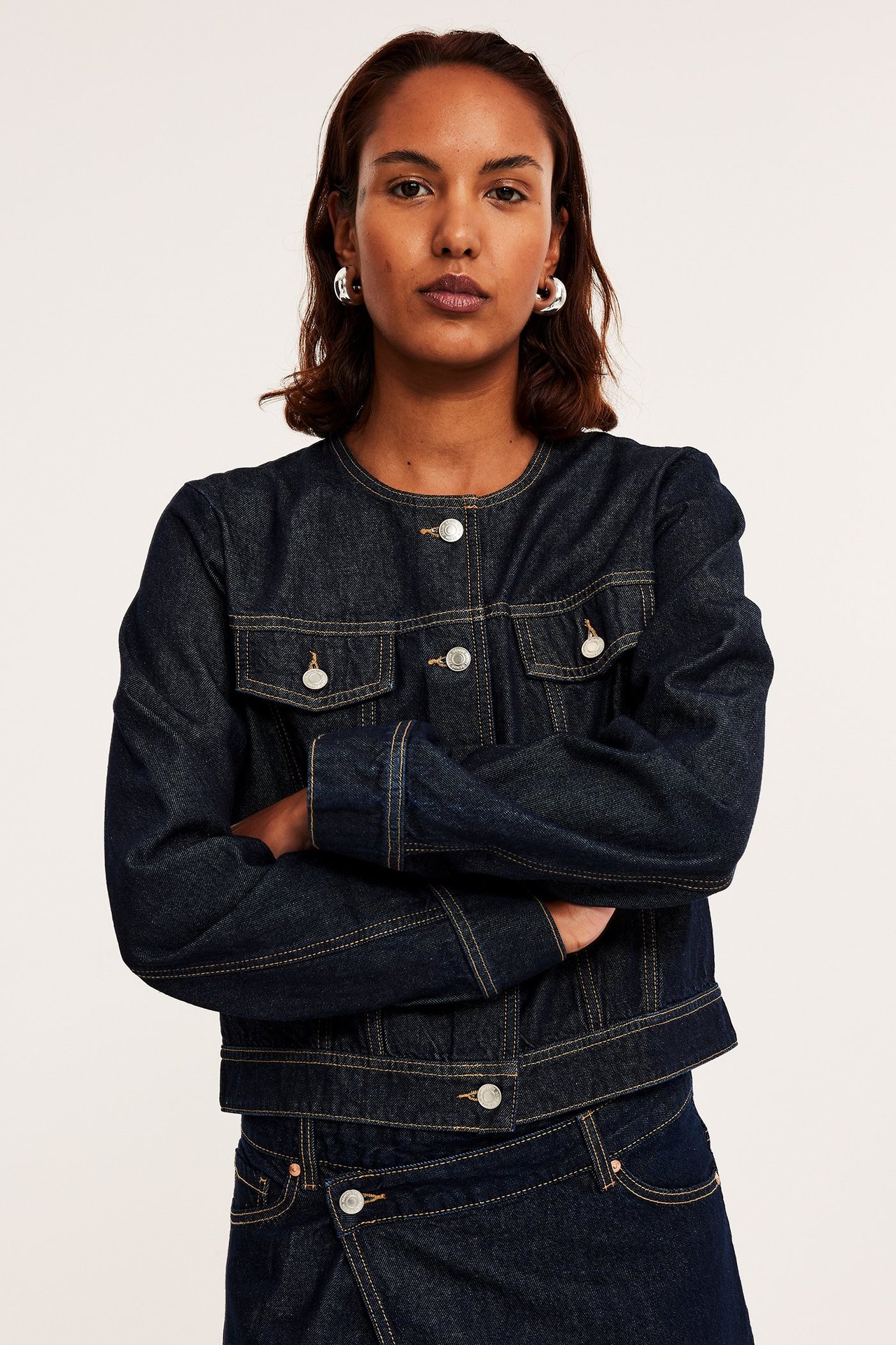 Frontbilde: Kvinne i mørk denim croppet jakke med vide ermer, sølvknapper og matchende denimskjørt.
