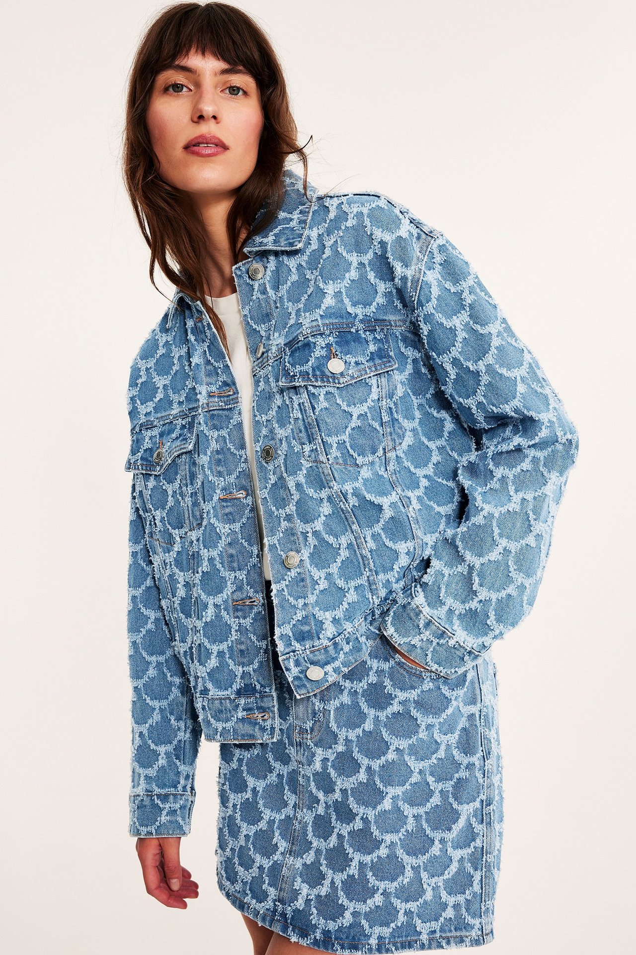 Forfra: Kvinne i blå kort jeansjakke med teksturert jacquardmønster og matchende skjørt.