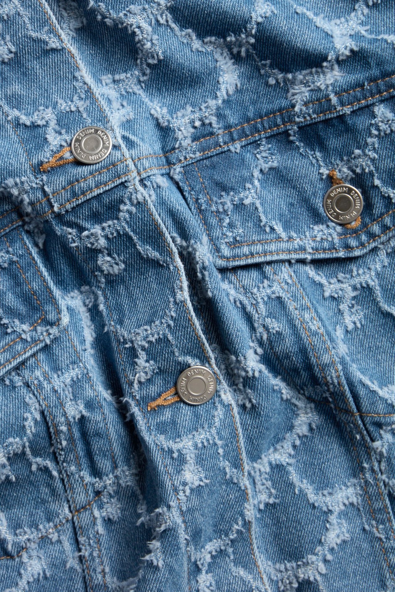 Zbliżenie niebieskiej kurtki jeansowej z teksturowanym wzorem żakardowym i srebrnymi guzikami.