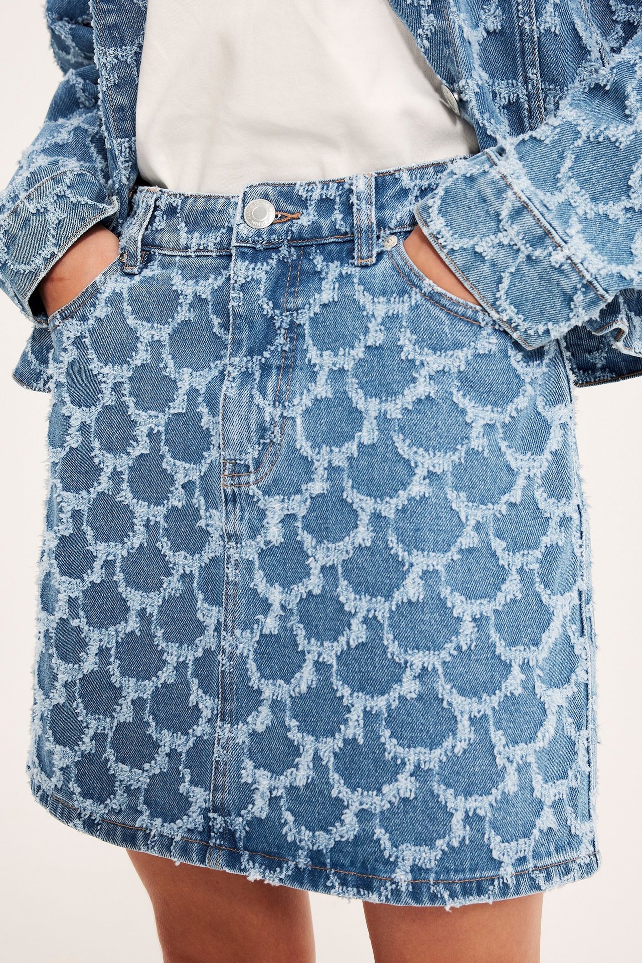 Frontvisning: Kvinne har på seg et kort blått jacquard-jeansskjørt, hvit t-skjorte og matchende jeansjakke.