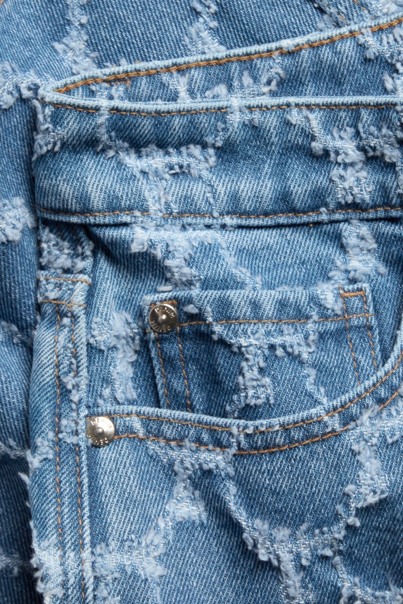 Zbliżenie na niebieską spódnicę jeansową z teksturowanym wzorem żakardowym, małą kieszenią i metalowym nitem.