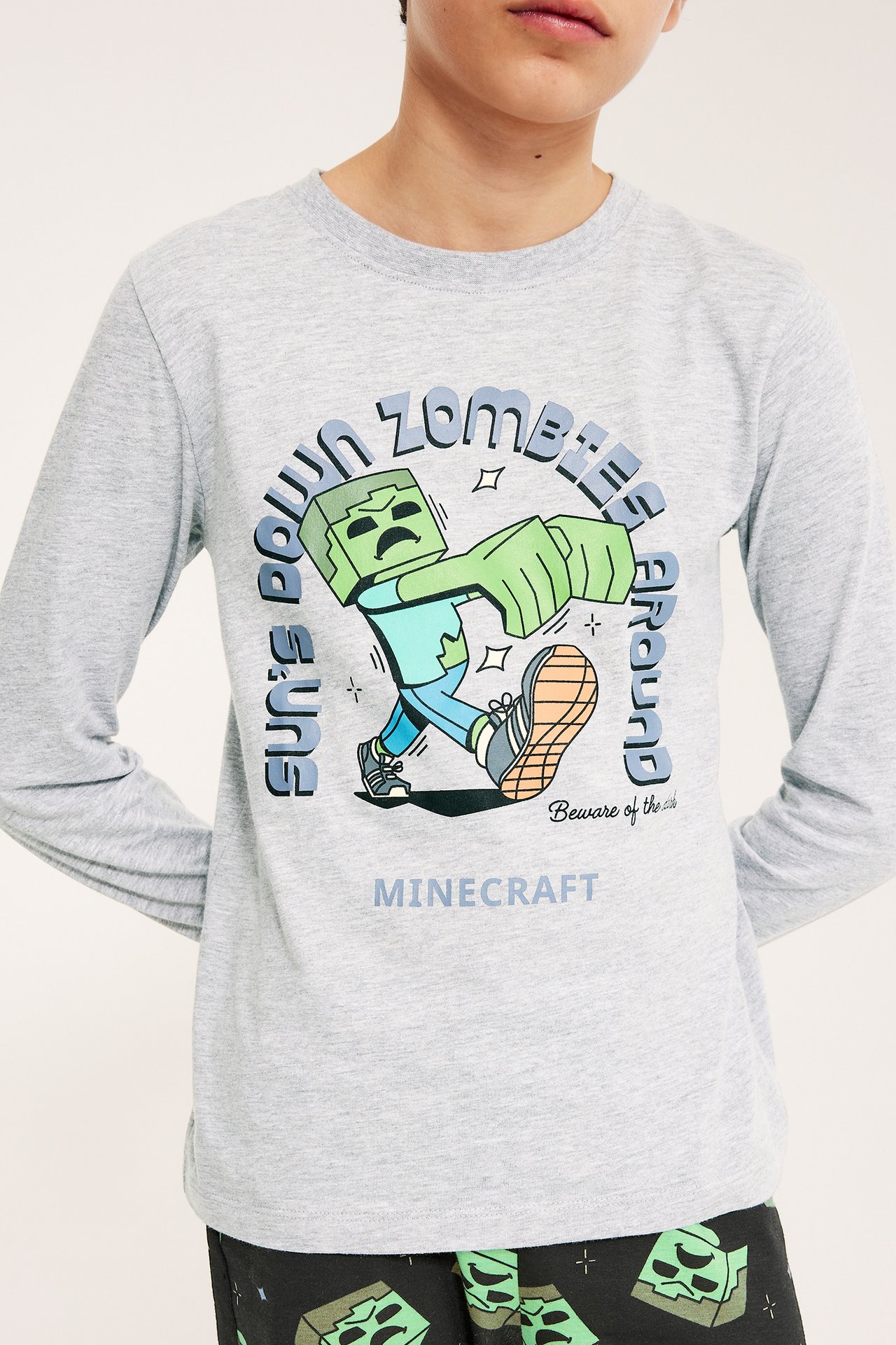 Edestäpäin: lapsi harmaassa pitkähihaisessa Minecraft-zombieprinttipaidassa ja mustissa kuvioiduissa pyjamahousuissa.